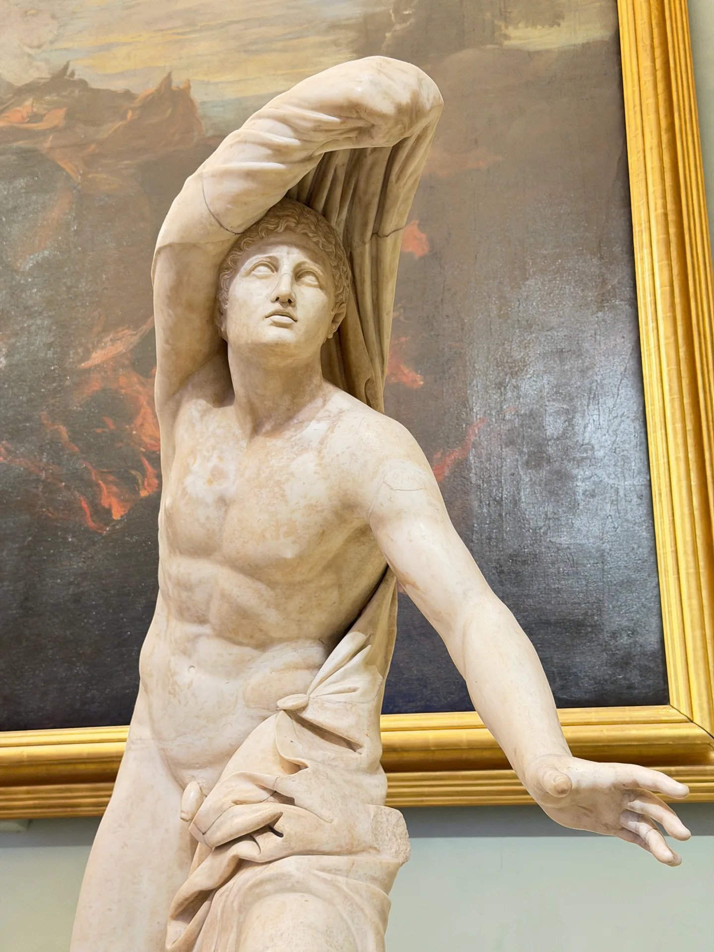 A son of Niobe pulling his mantle up over his head, lit against the dark canvas behind.