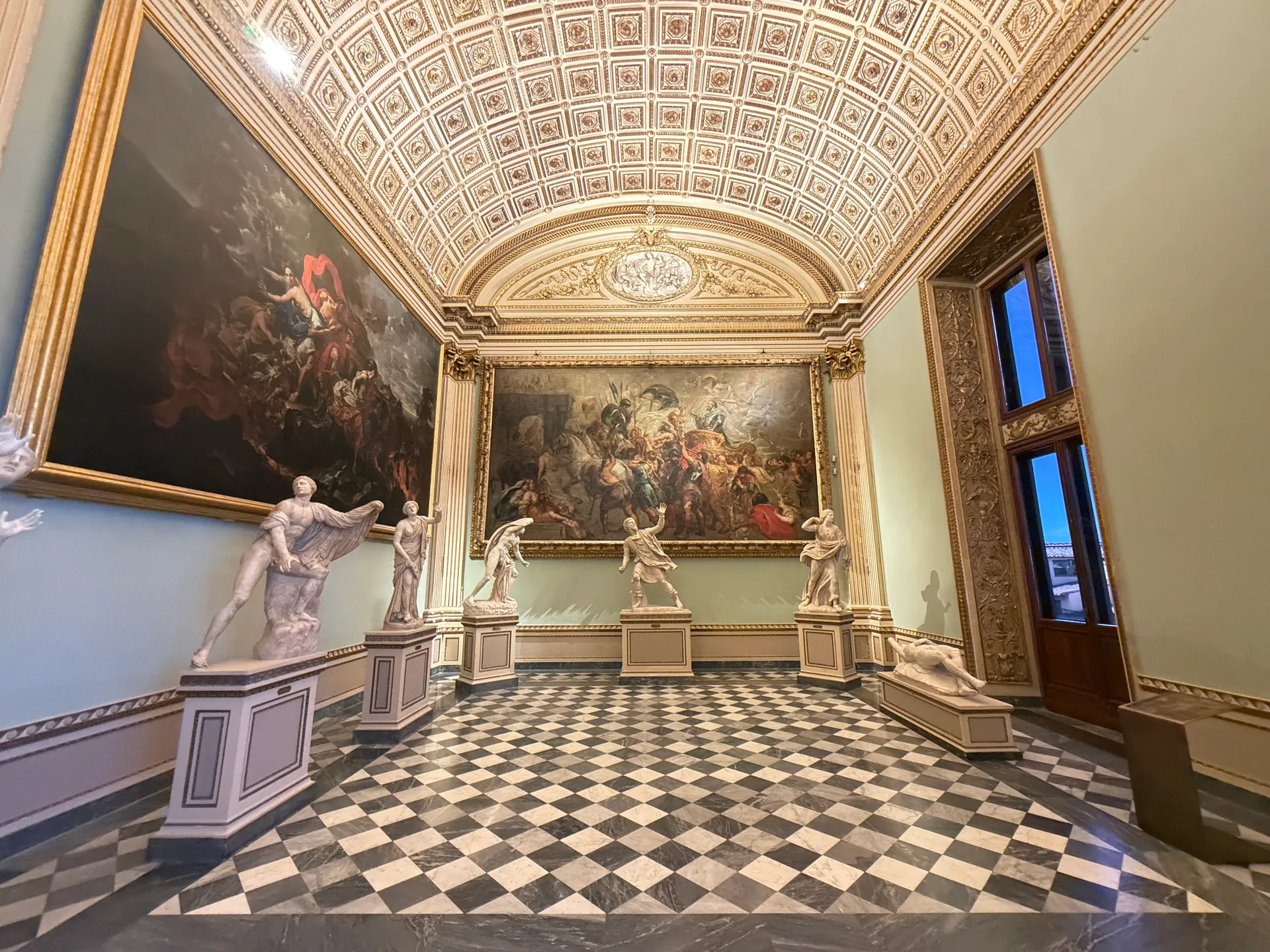 The Sala della Niobe, pale coffered vault above a black and white checkerboard floor, standing empty.