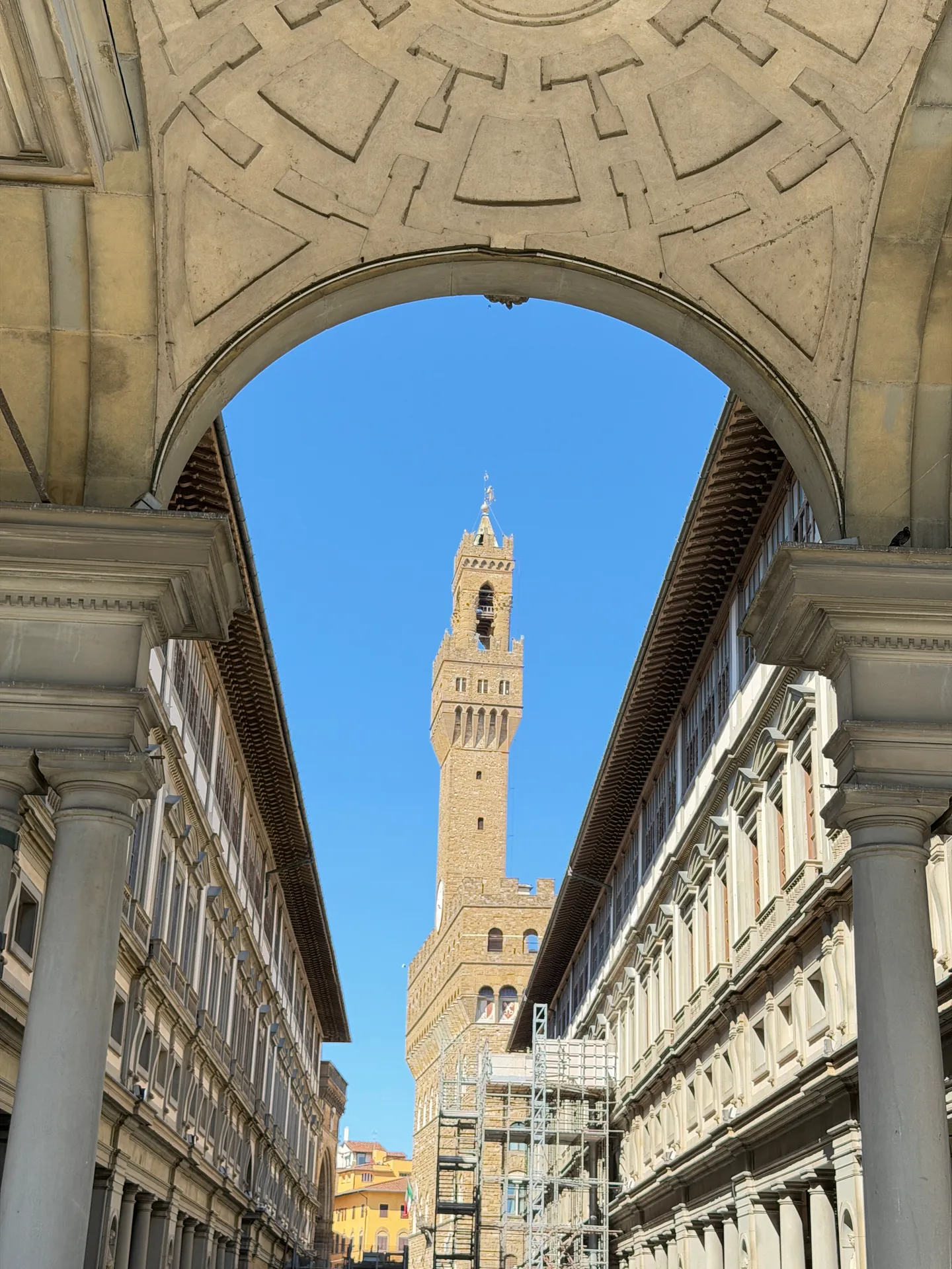 The arch closing the Arno end of the Uffizi courtyard, framing the Palazzo Vecchio tower at the far end.
