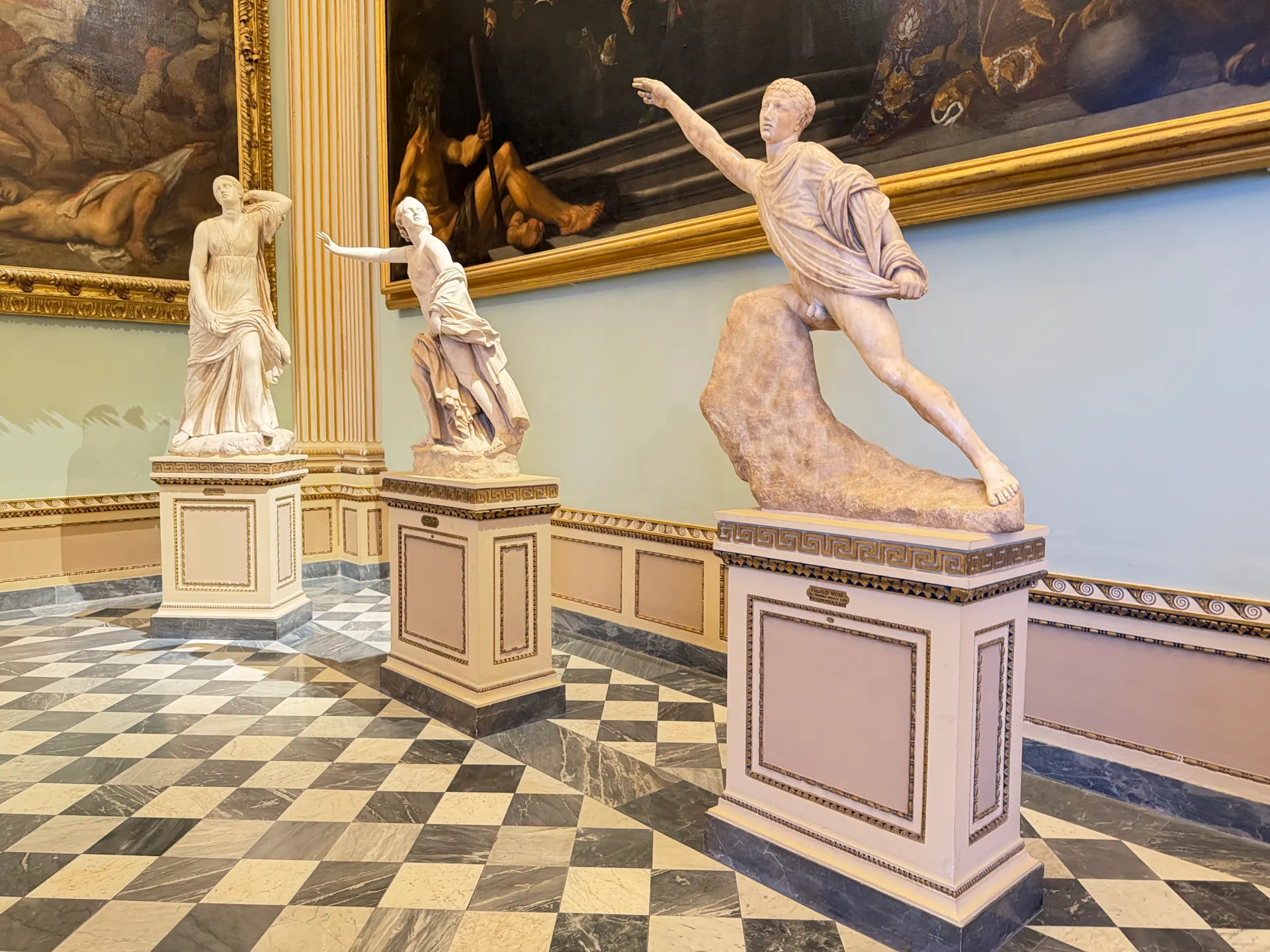 Three Niobid statues ranged along the wall of the Sala della Niobe above the checkerboard floor.