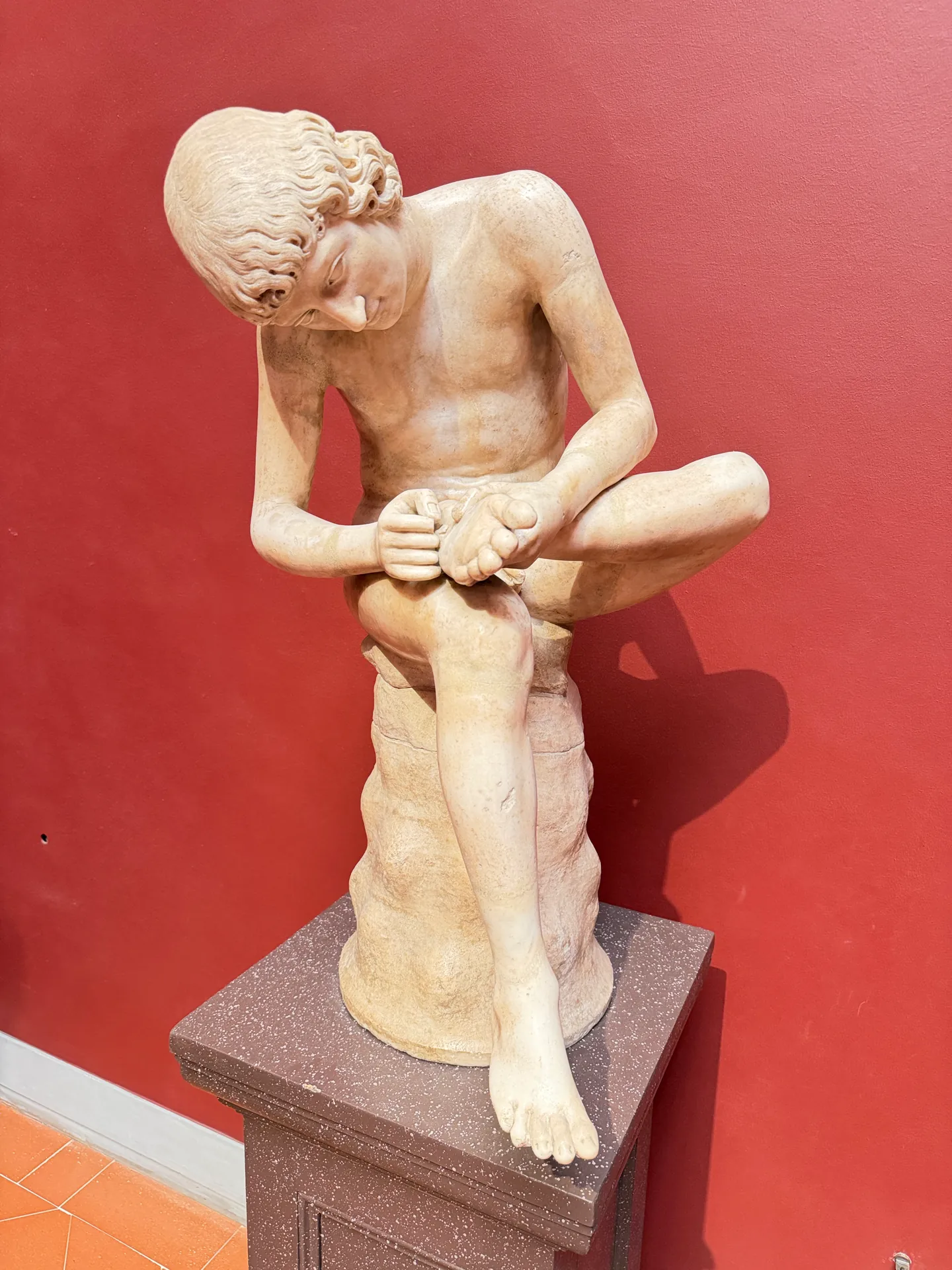 An antique marble of a seated boy bent forward to pull a thorn from his foot.