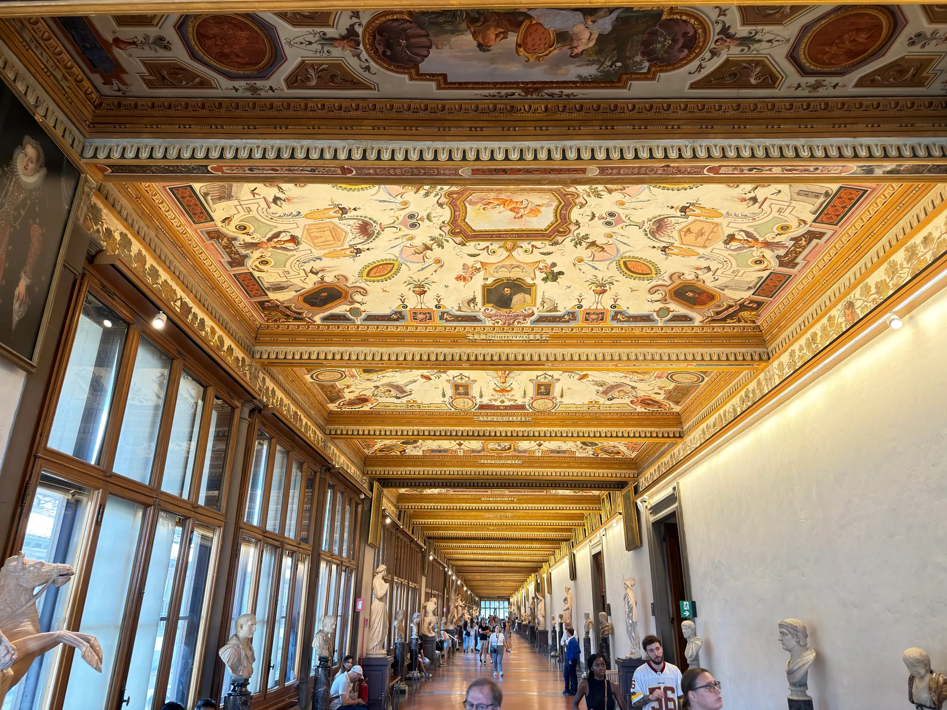The Uffizi's third corridor seen down its length, grotesque painted ceiling above and antiquities along both walls.