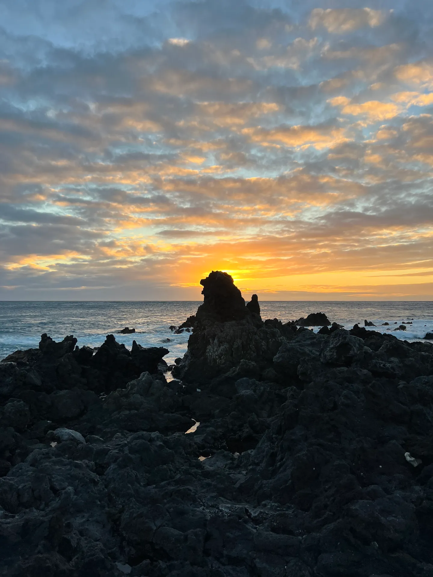 A lava outcrop silhouetted against an orange sunset over the sea