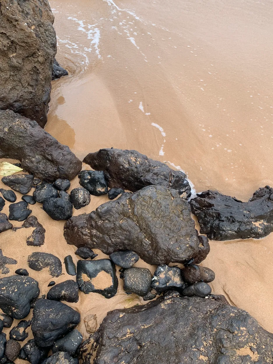 Dark lava boulders on sand at the edge of the shore