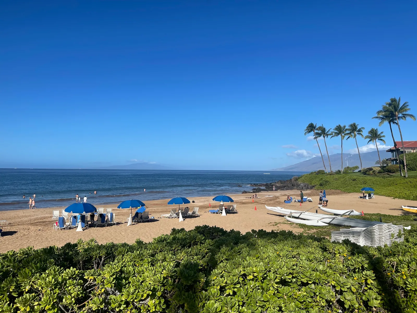 Polo Beach with outrigger canoes on the sand, blue umbrellas and swimmers in the shallows