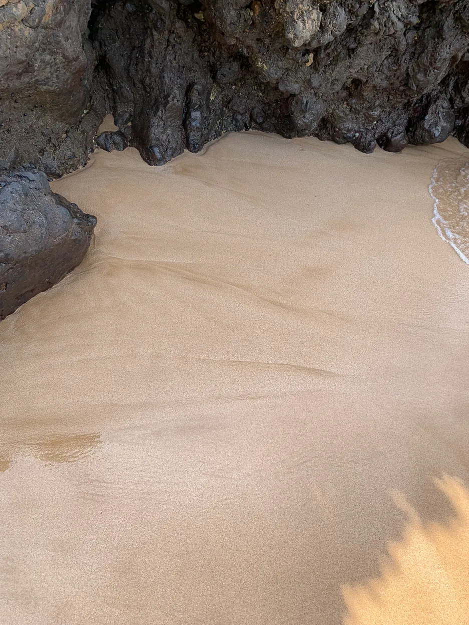 Dark volcanic rock overhang above pale sand at the shoreline