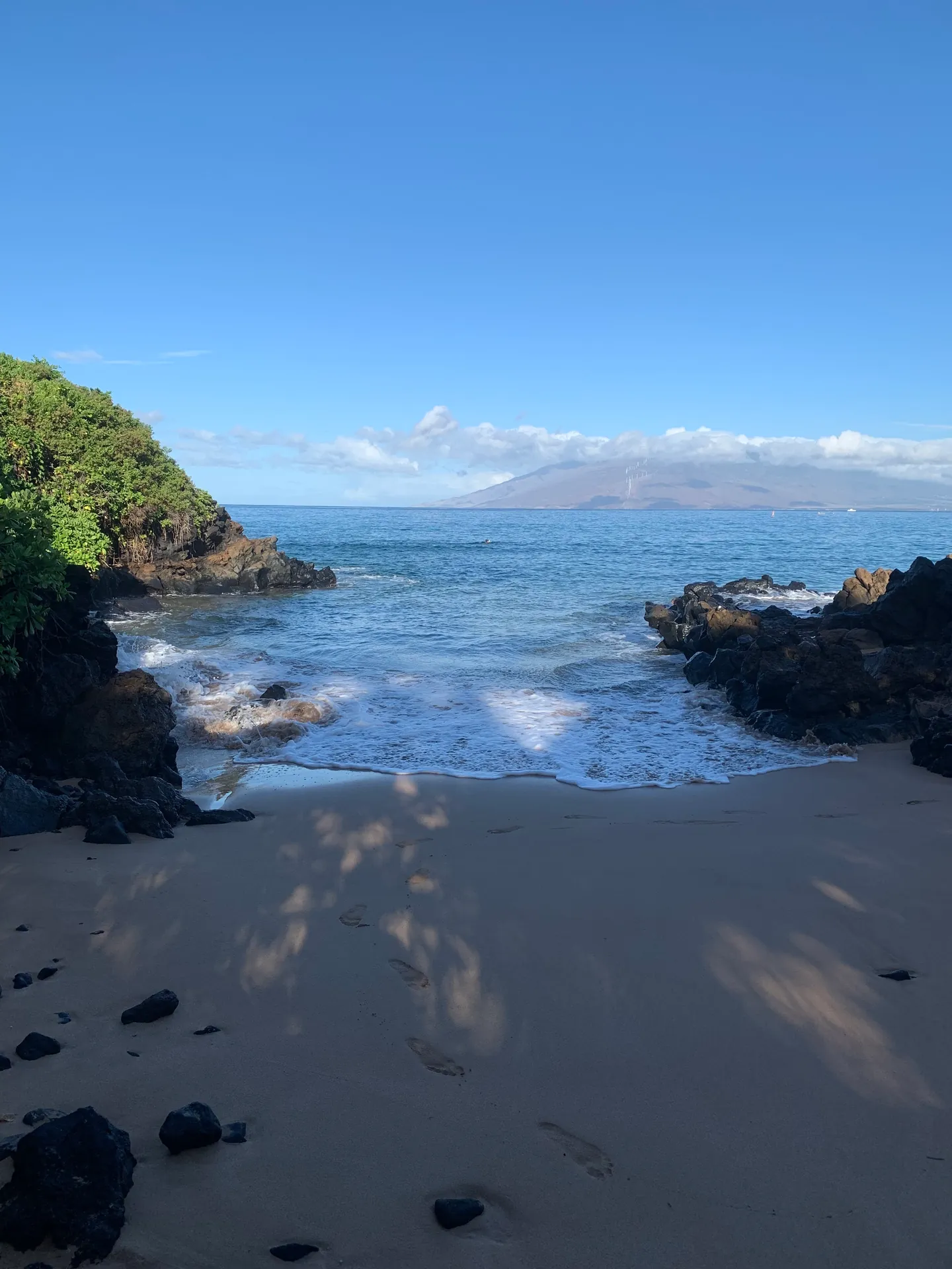 Small sandy cove between lava outcrops with mountains across the water beyond