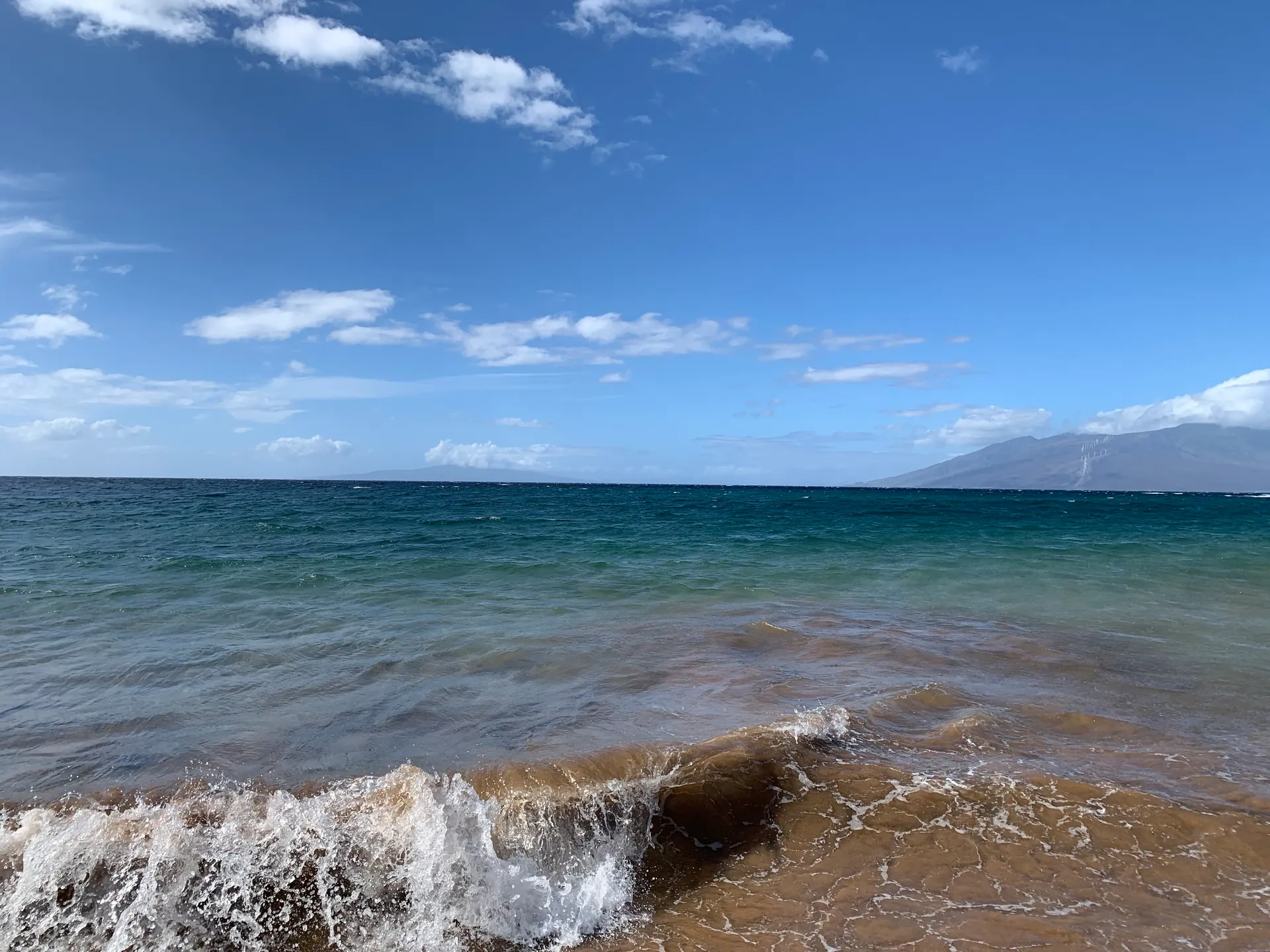 Small waves breaking onto a sandy beach under a bright sky