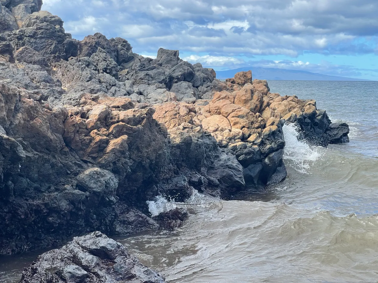 White water breaking against dark lava rock beside sand
