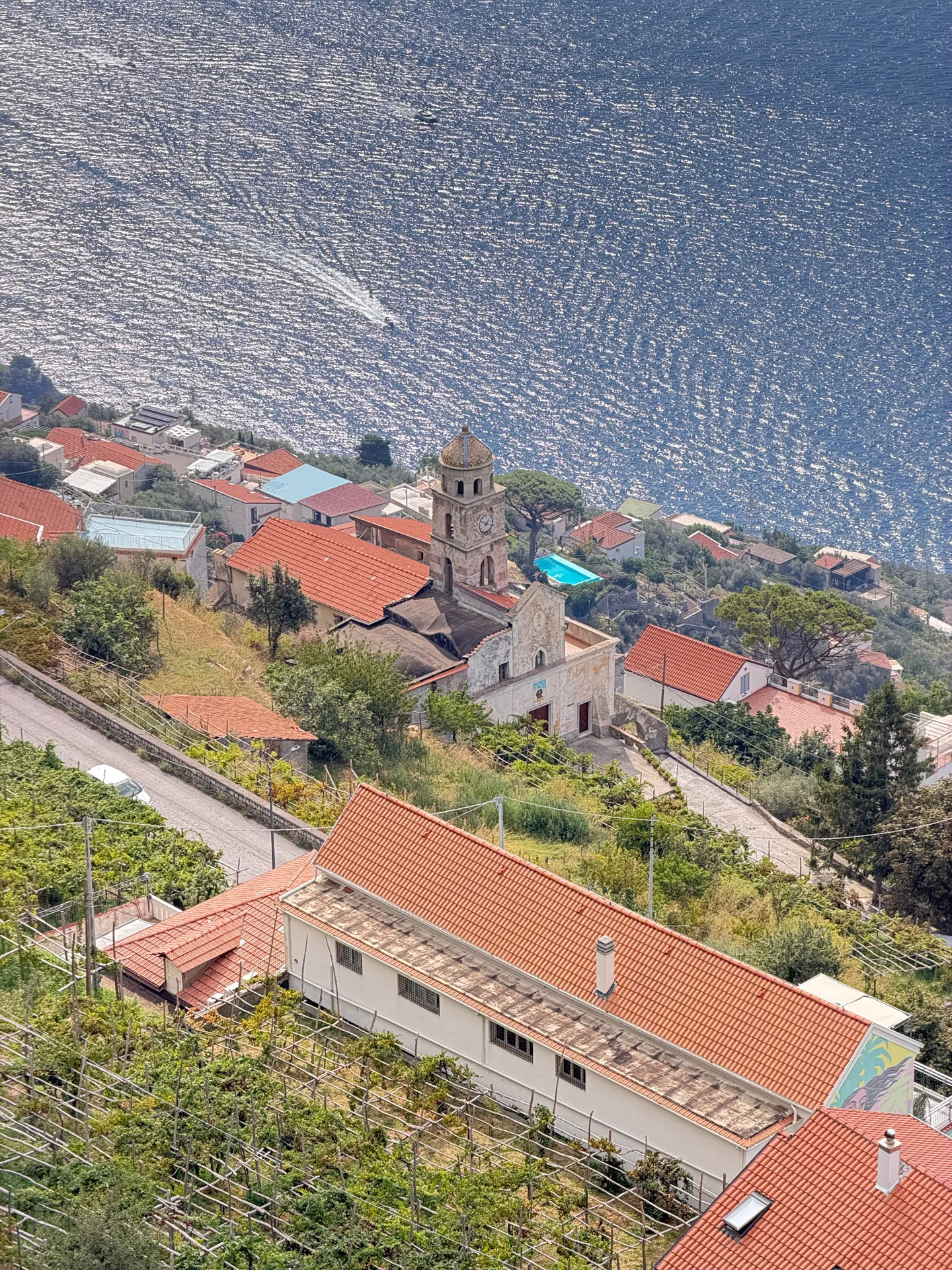 A village bell tower and red roofs on the shoreline far below, seen with a telephoto lens