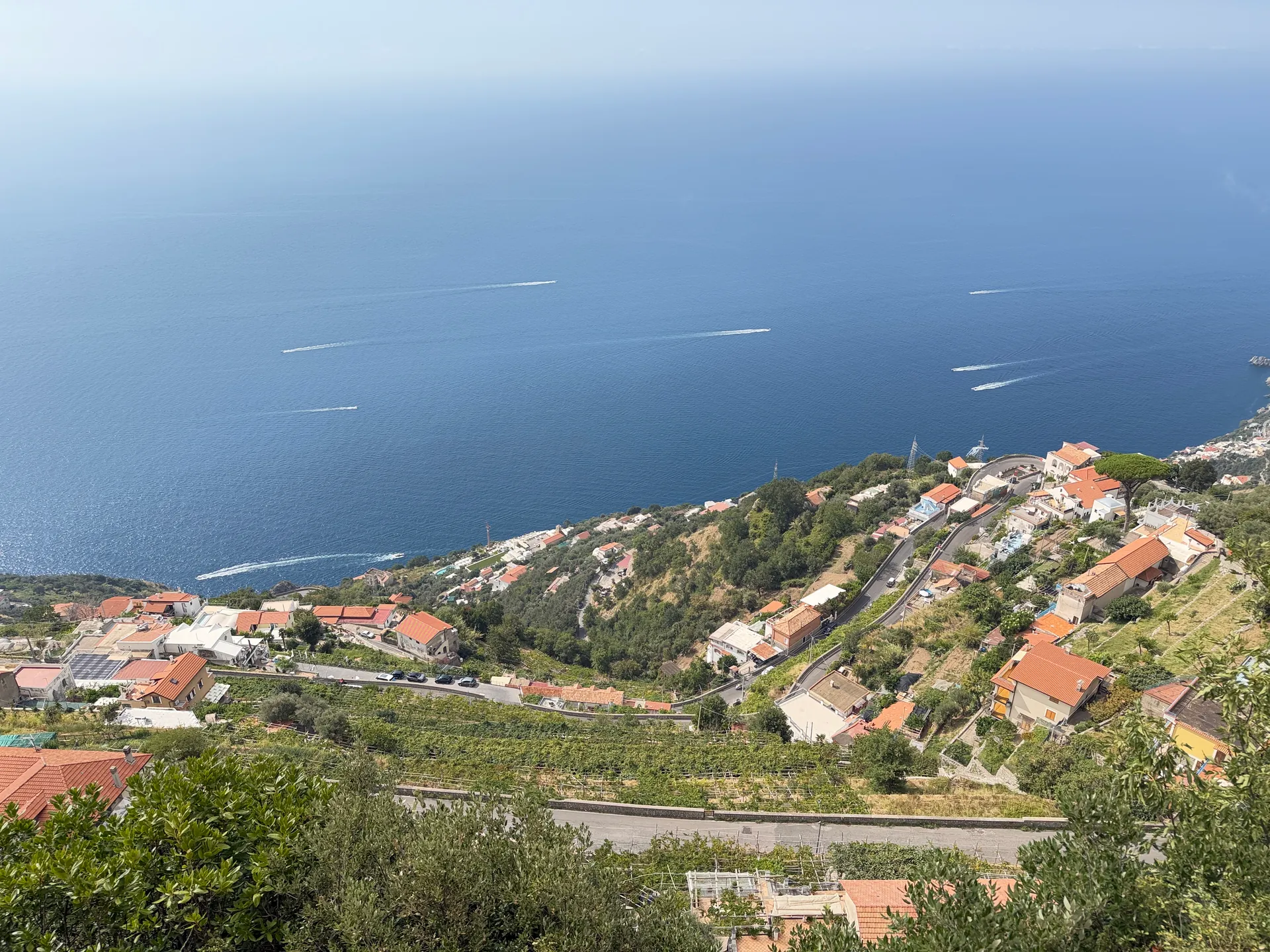 A steep hillside of terraces and red-roofed houses falling away to the sea seen from high above