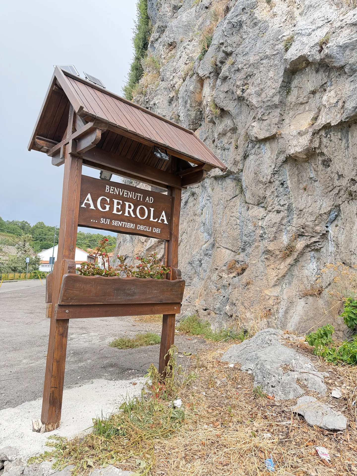A wooden sign reading Agerola under a bare limestone rock face beside the road