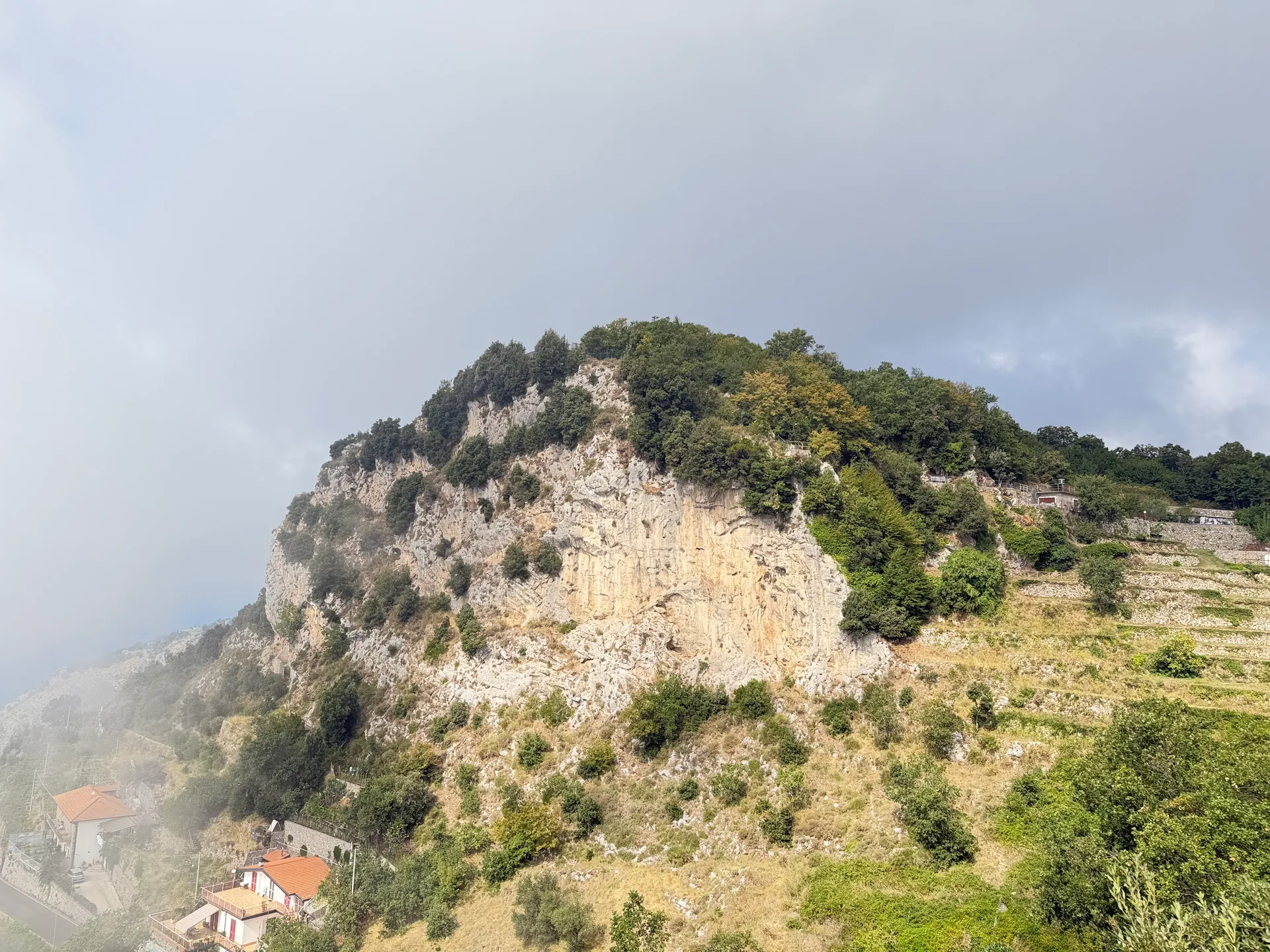 A pale limestone crag above green terraces in full sun under a partly clouded sky