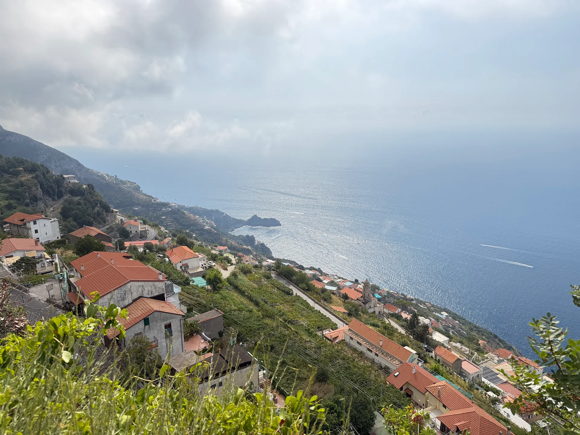 Terraced slopes and rooftops leading toward a coastal headland with pale sea behind