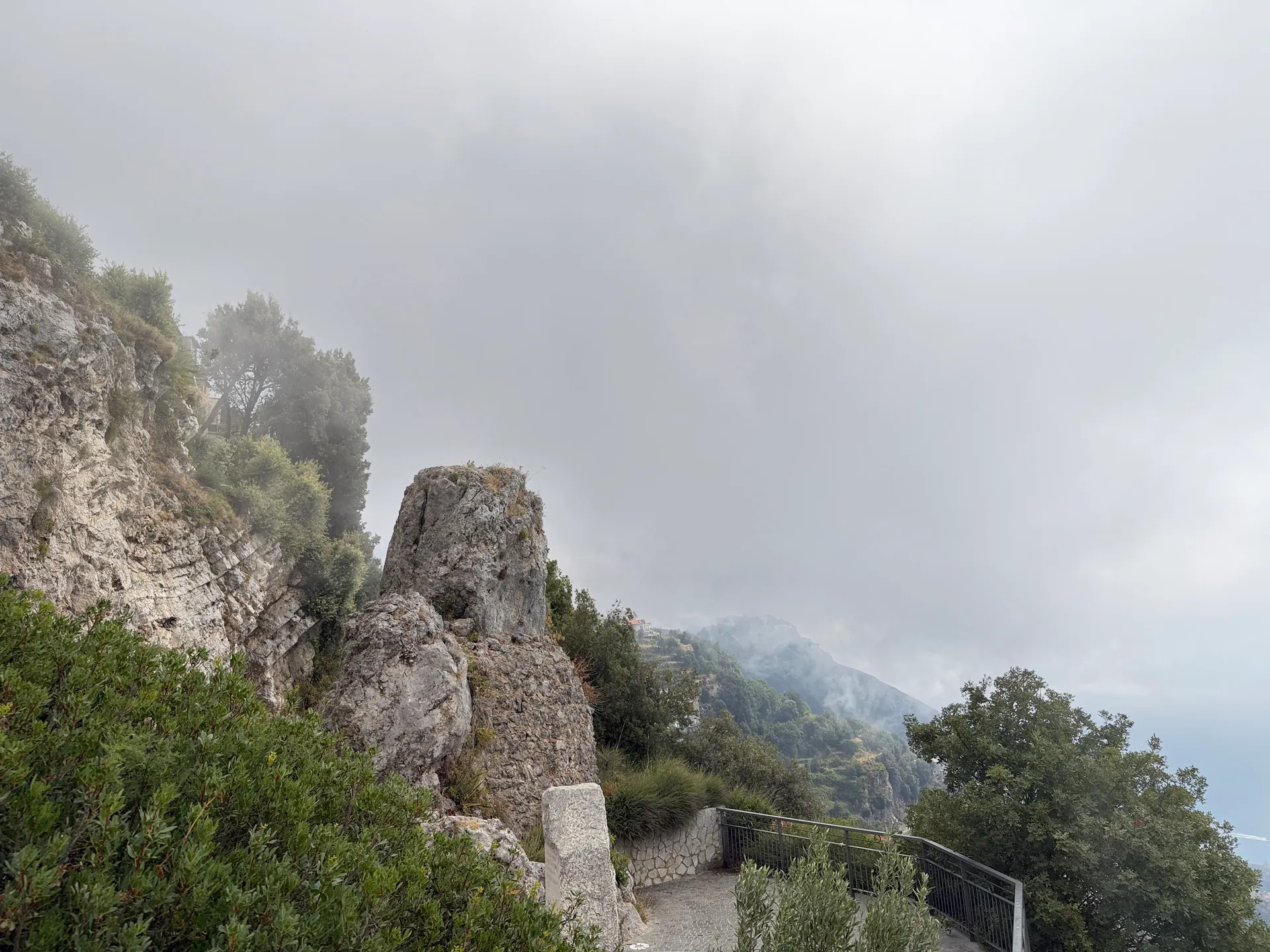 Rock pinnacles beside a road barrier emerging from cloud, more cloud behind
