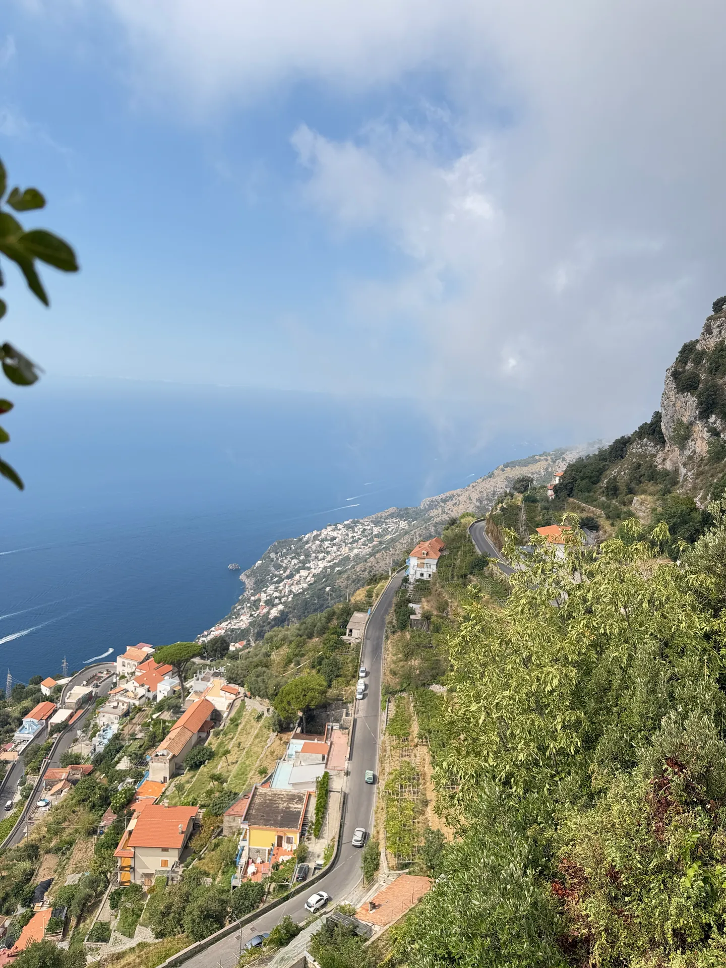 A road switchbacking down a steep coastal hillside past scattered houses, sea beyond