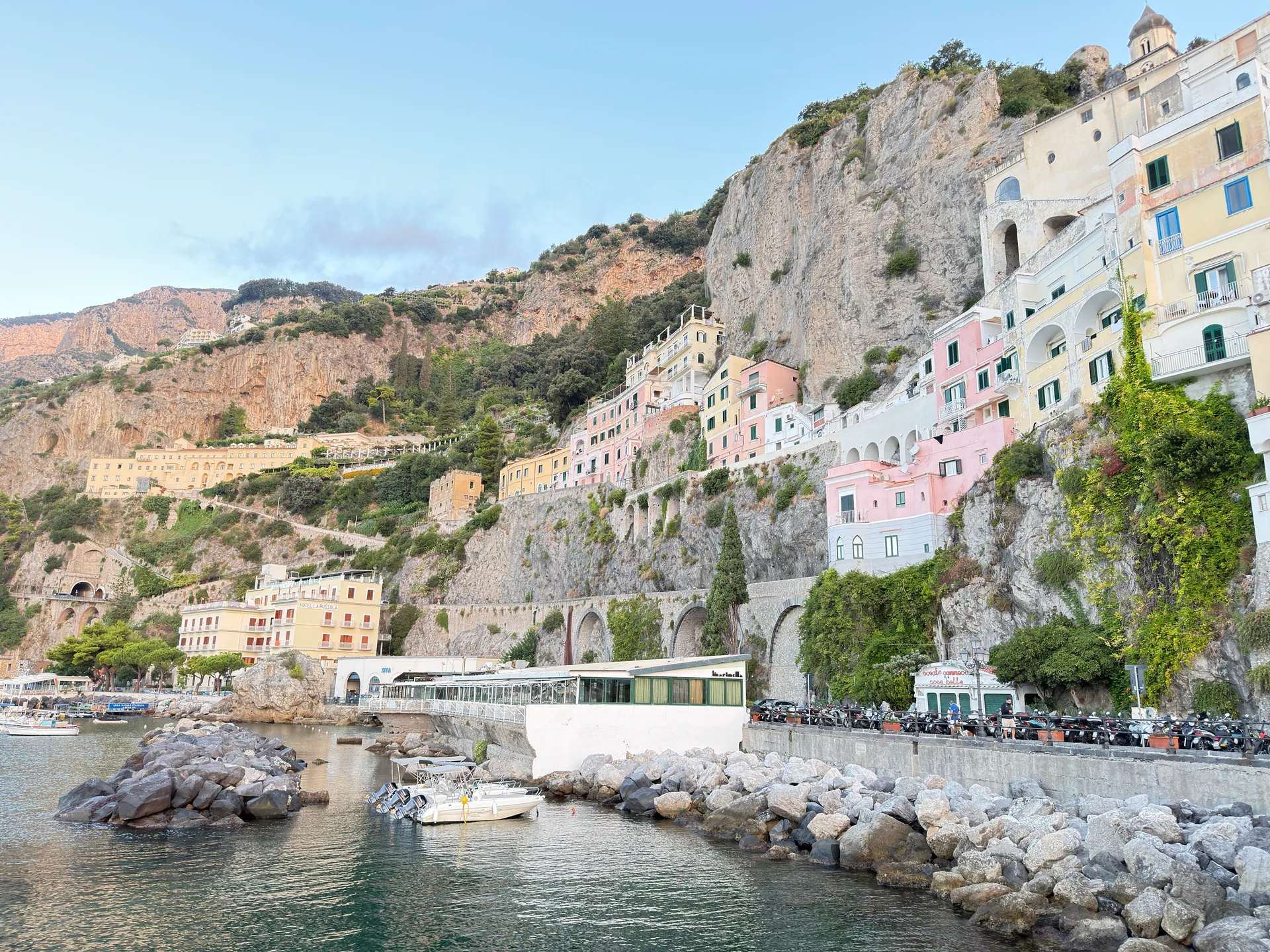 Pastel houses stacked up a limestone cliff above a rocky shore and a road