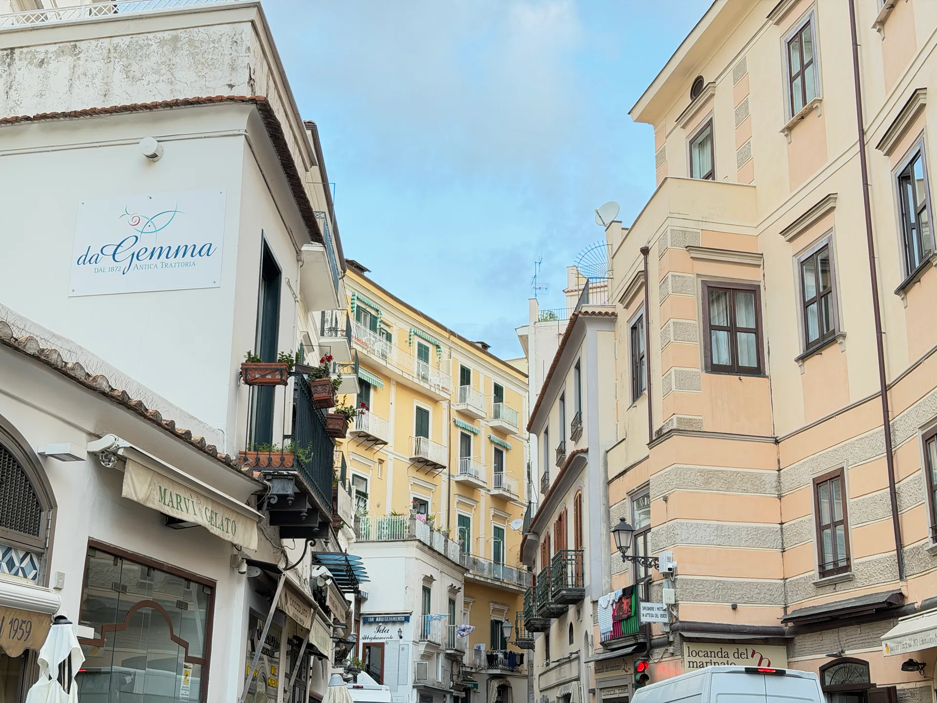 Street corner with a white sign for the da Gemma trattoria and yellow houses beyond