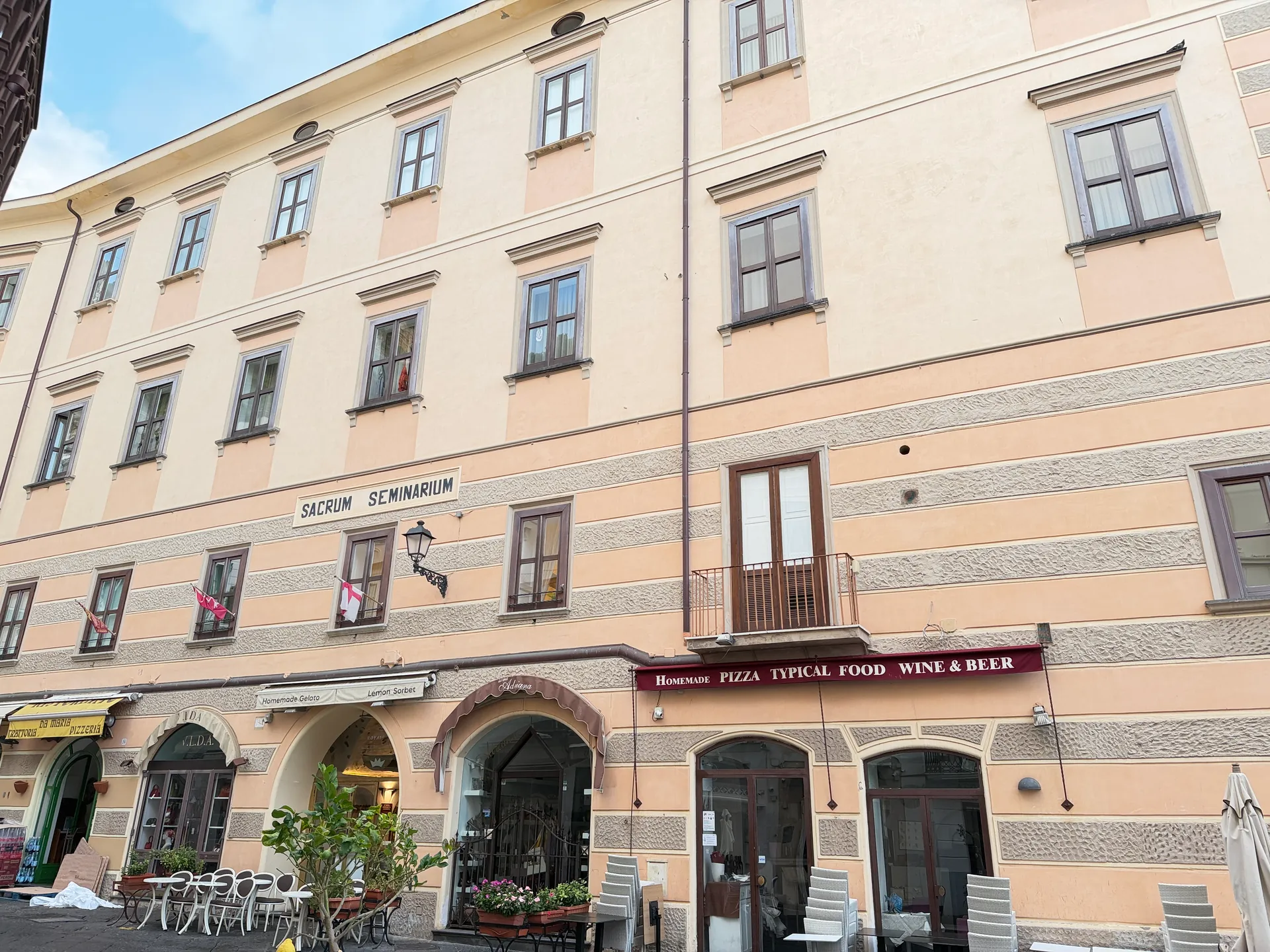 Striped facade with a carved tablet reading Sacrum Seminarium above a pizzeria awning