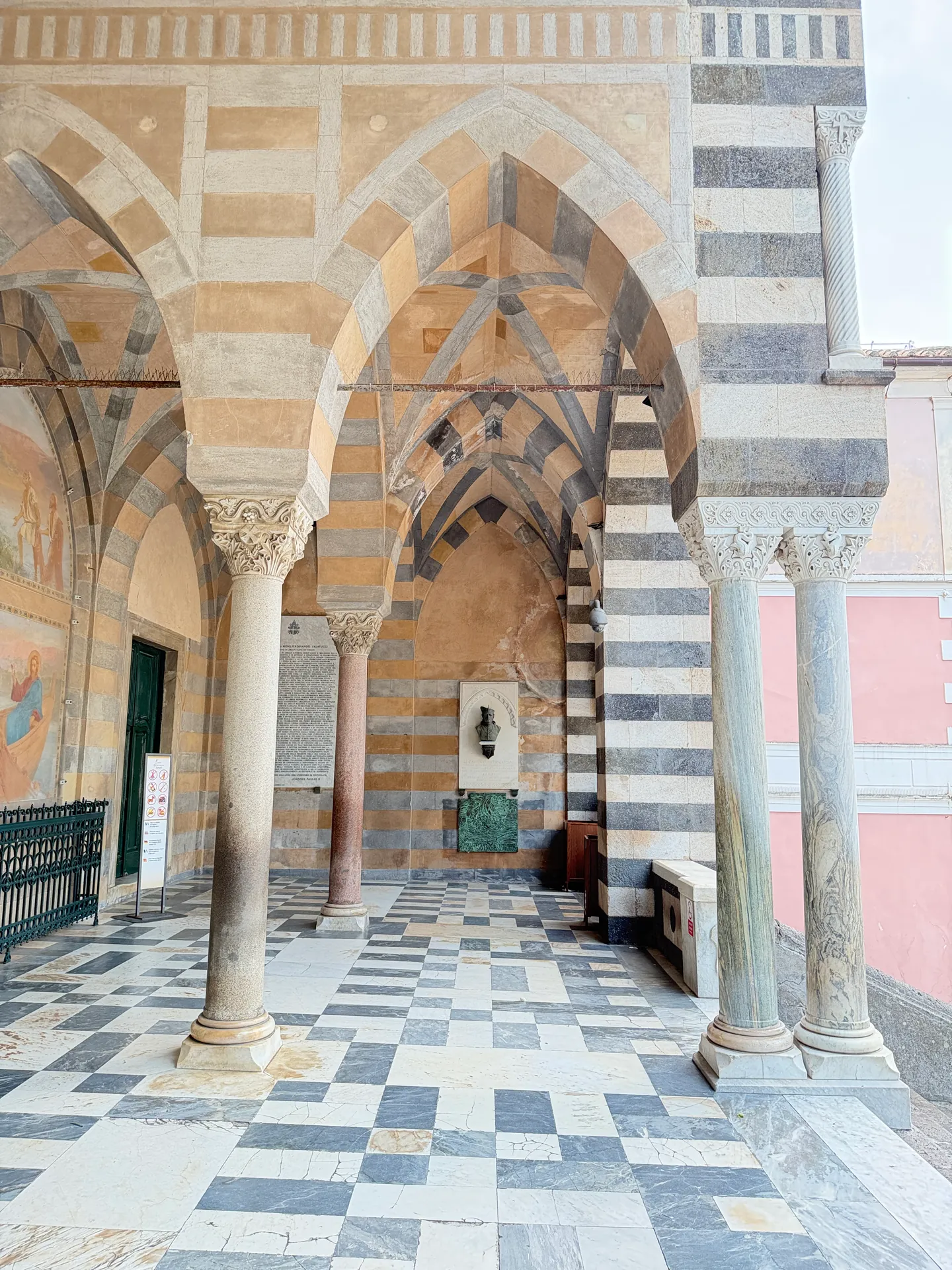 Atrium wall of Amalfi cathedral with a marble memorial and an inscribed panel between striped pointed arches