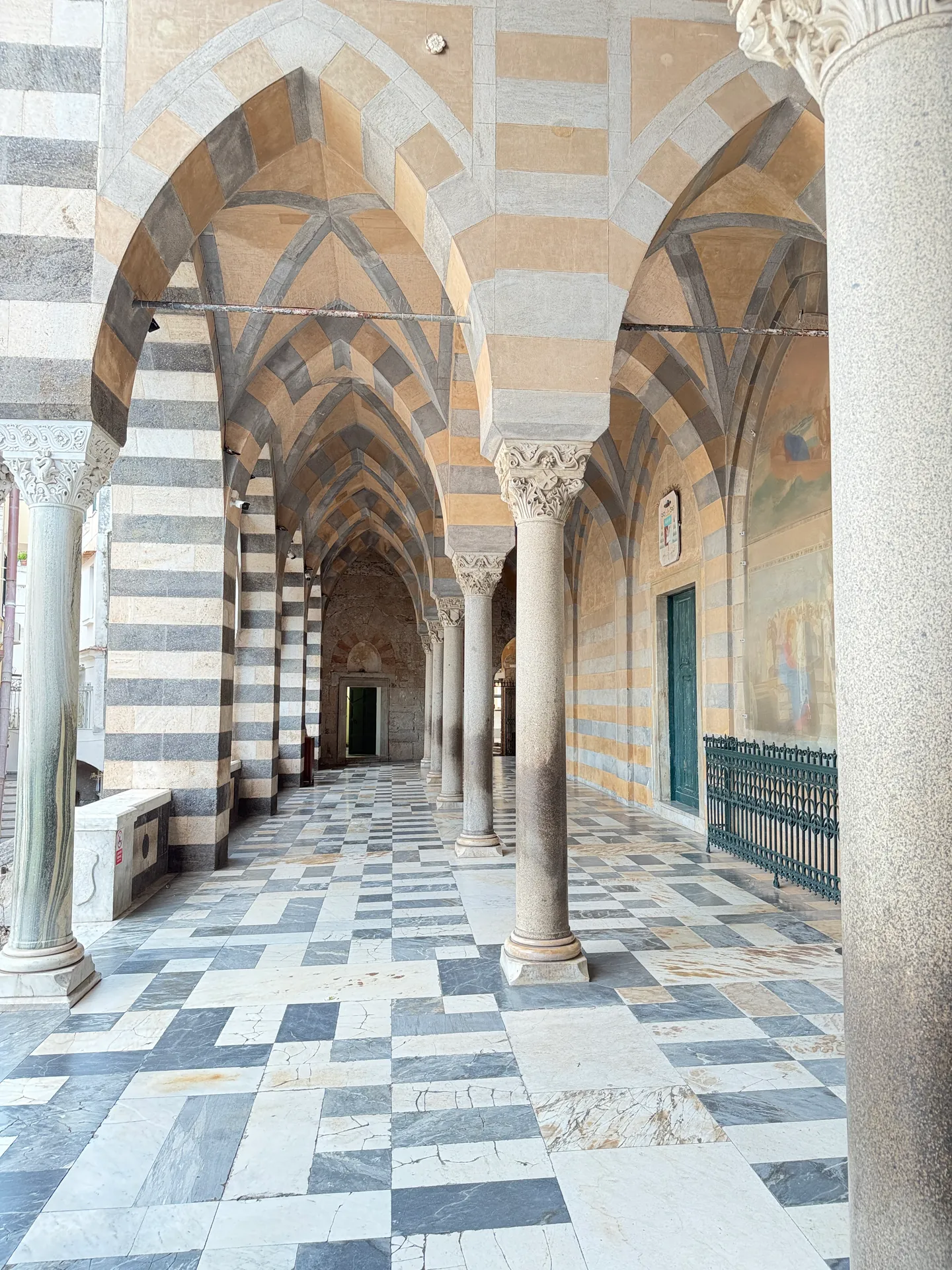 Striped pointed arches on stone columns over a chequered marble floor in the atrium of Amalfi cathedral