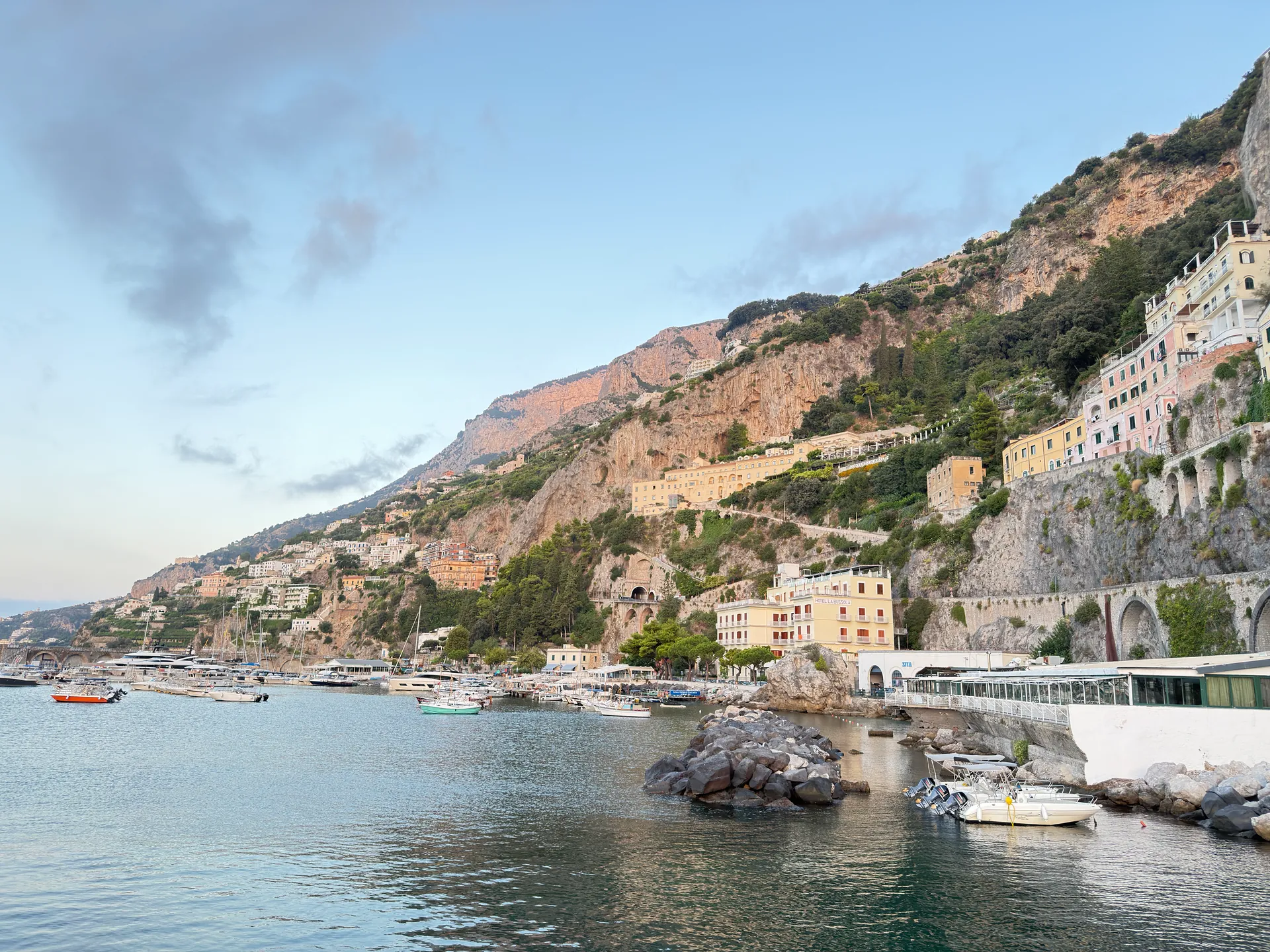 Rocky cove with moored boats below cliffside houses on a coastal shore at dawn
