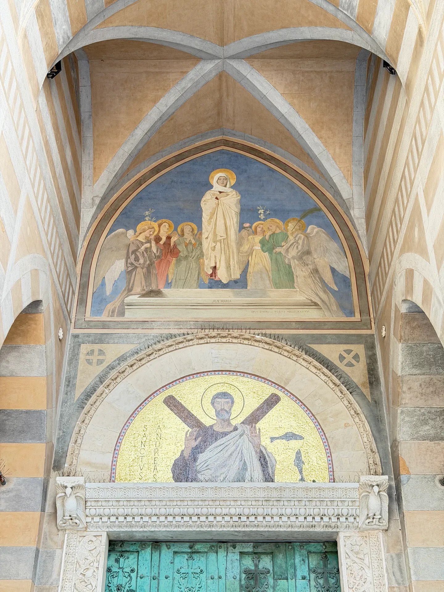 Two gold mosaic lunettes above the bronze door of Amalfi cathedral, under striped pointed arches