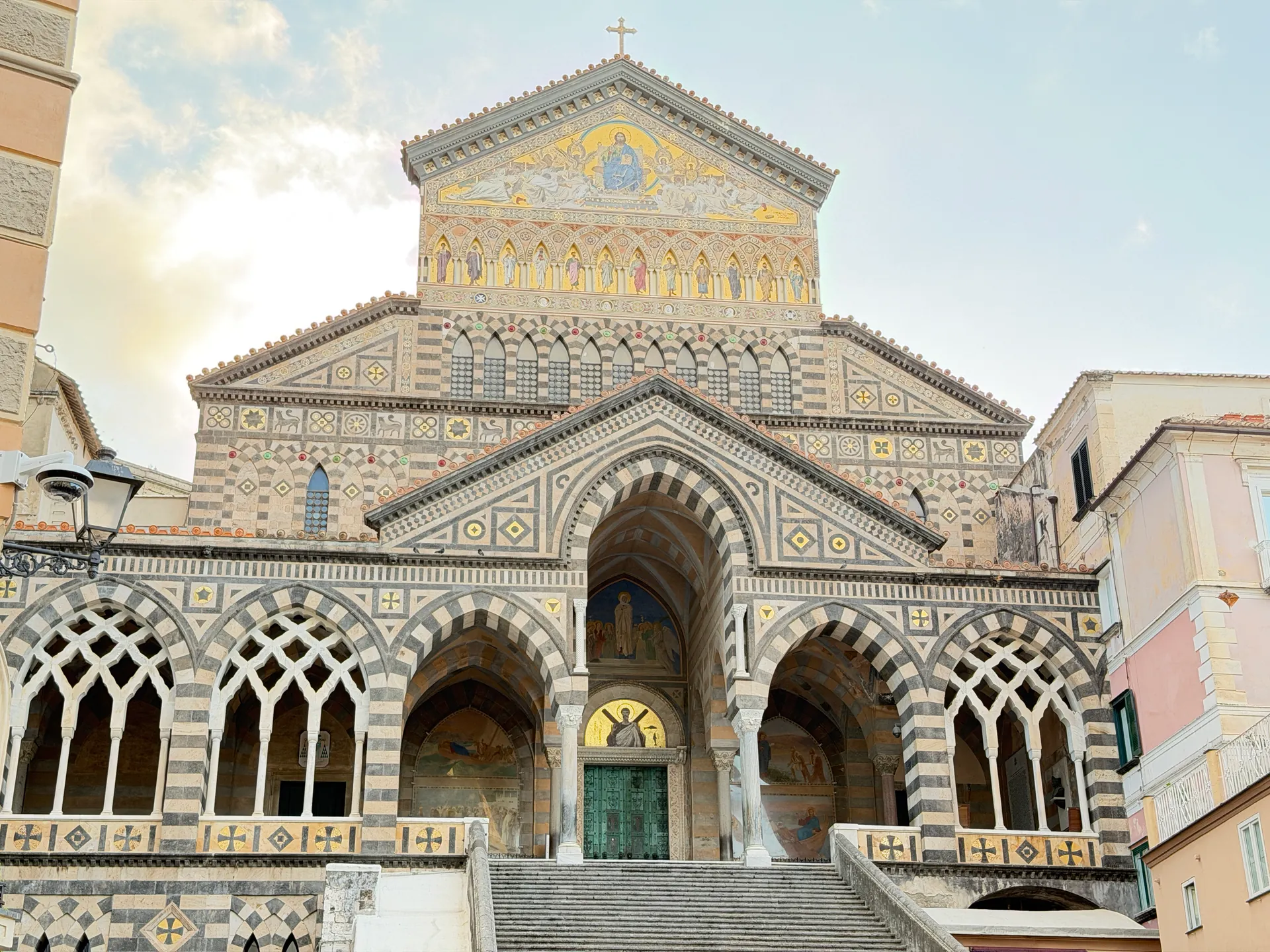 The striped facade of Amalfi cathedral with its gold mosaic pediment and pointed arches above the staircase