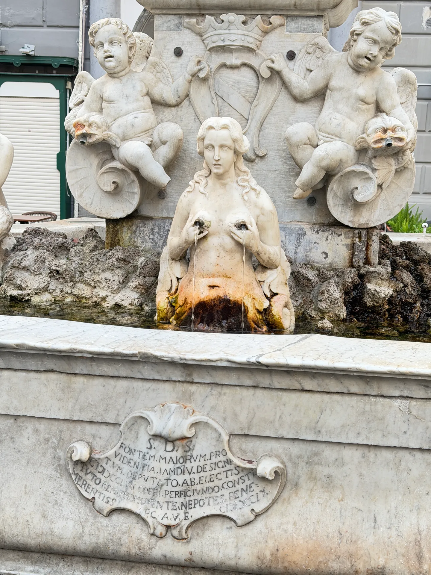 Carved marble cartouche with a Latin inscription below a siren and two cherubs on a fountain basin