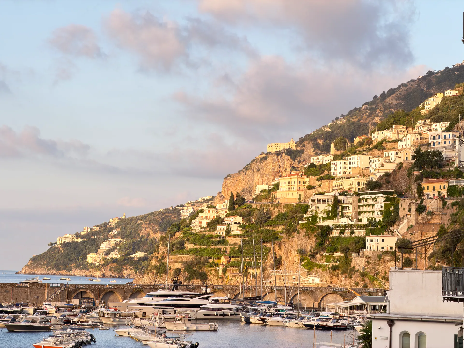 Amalfi marina and hillside town under a wide morning sky with lit clouds