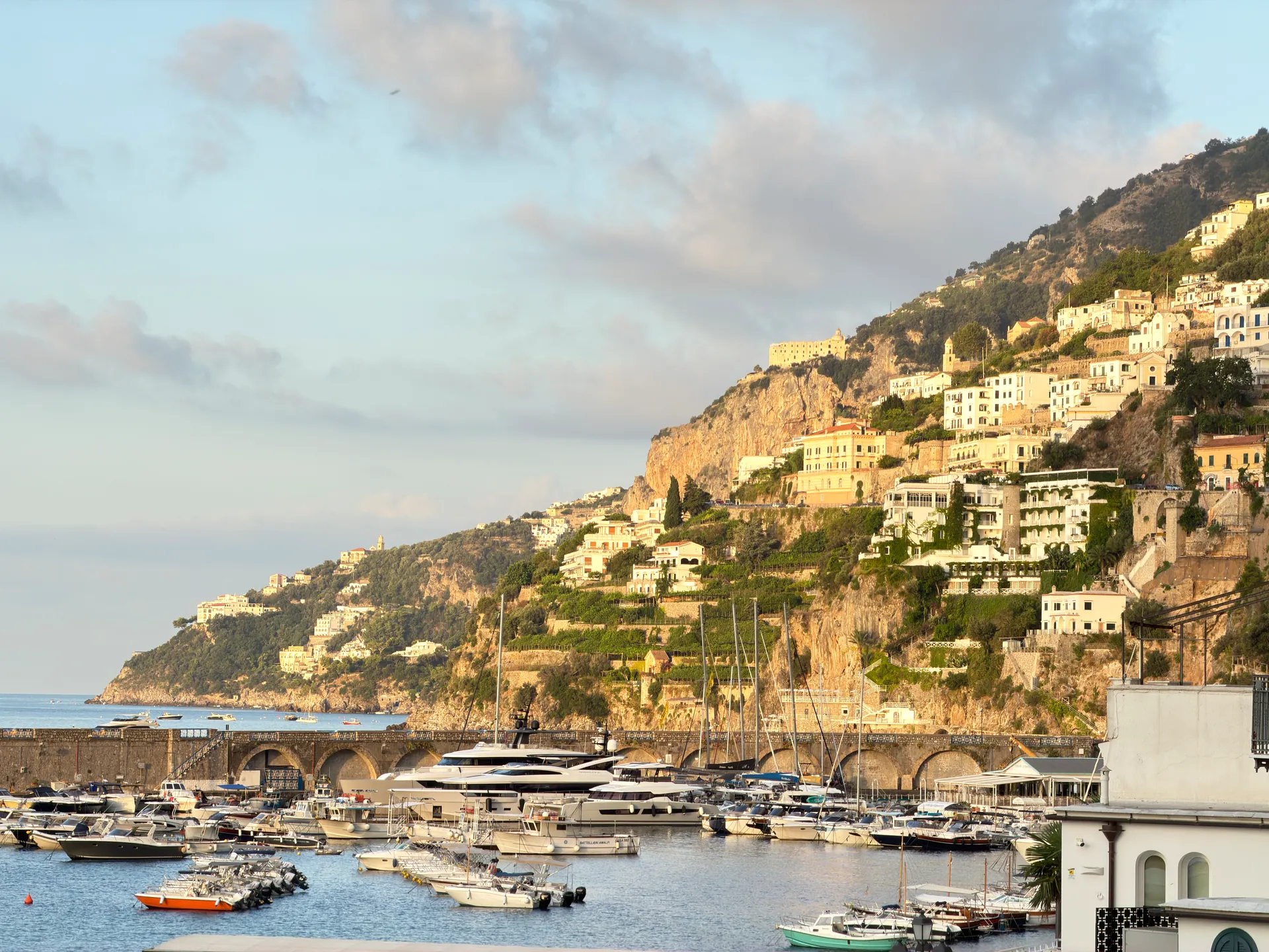 Boats moored in Amalfi marina below hillside houses in early morning light