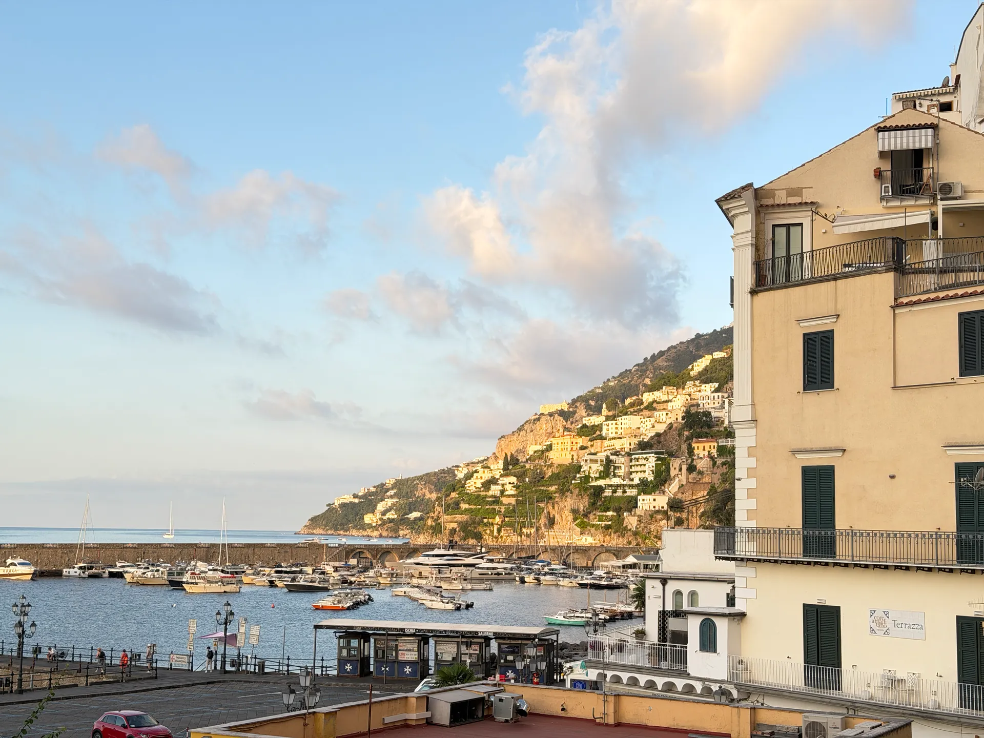 Stone mole and marina of Amalfi below a hillside of houses, quay and lamps in the foreground