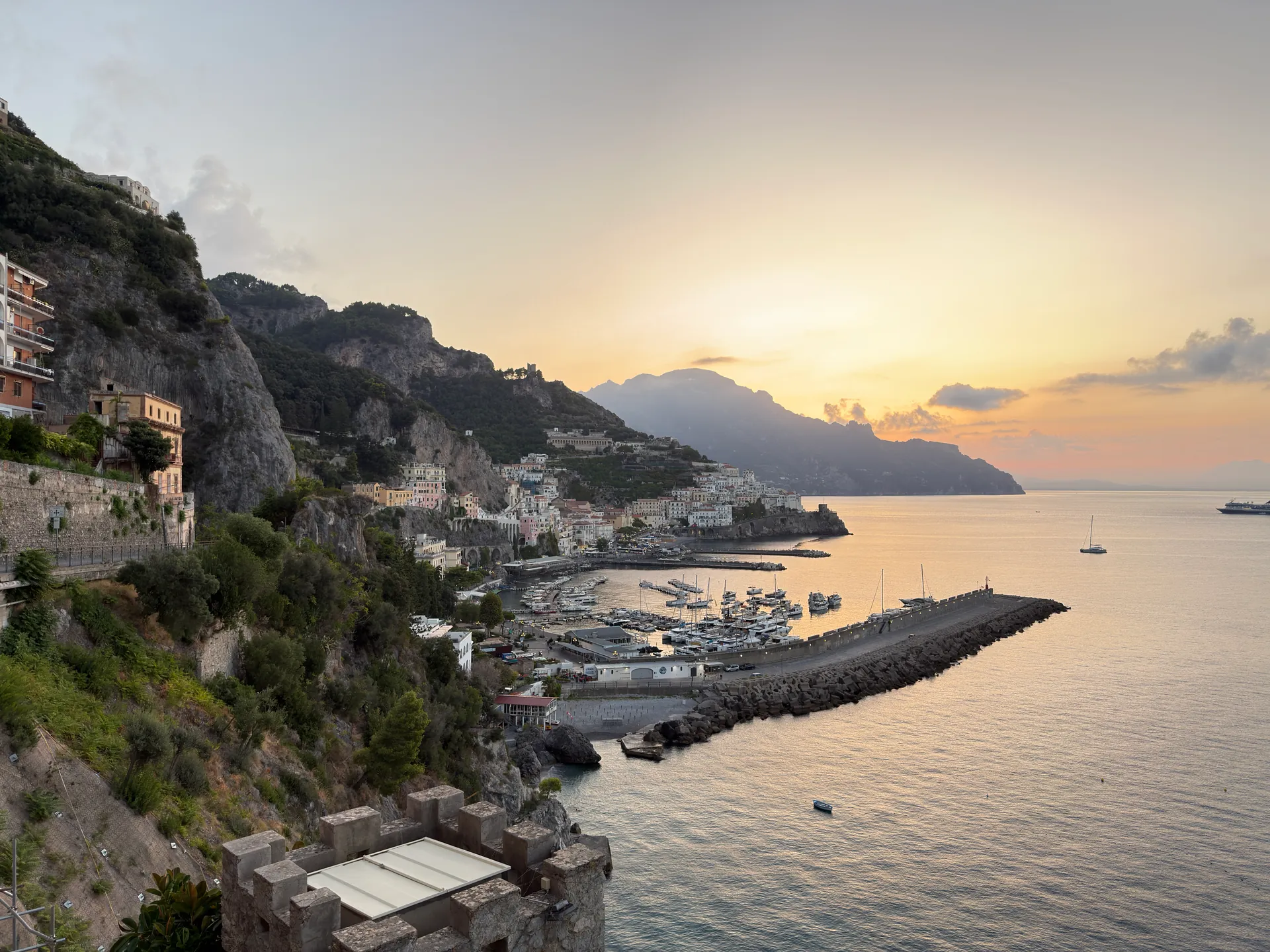 Stone mole and harbour of Amalfi at sunrise, seen past a crenellated tower on the point