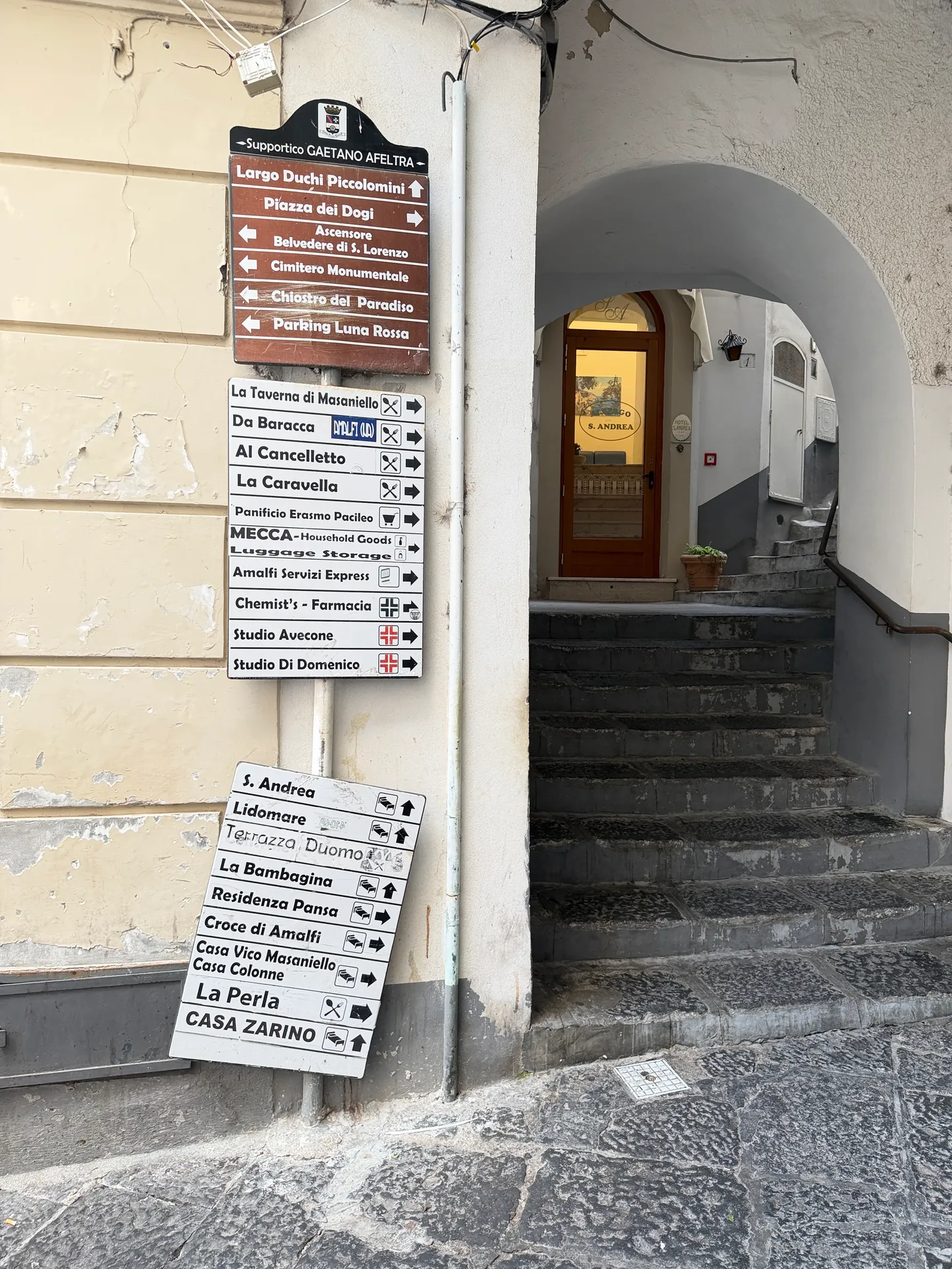 Cluster of white and brown direction signs on a wall beside an arched stair passage