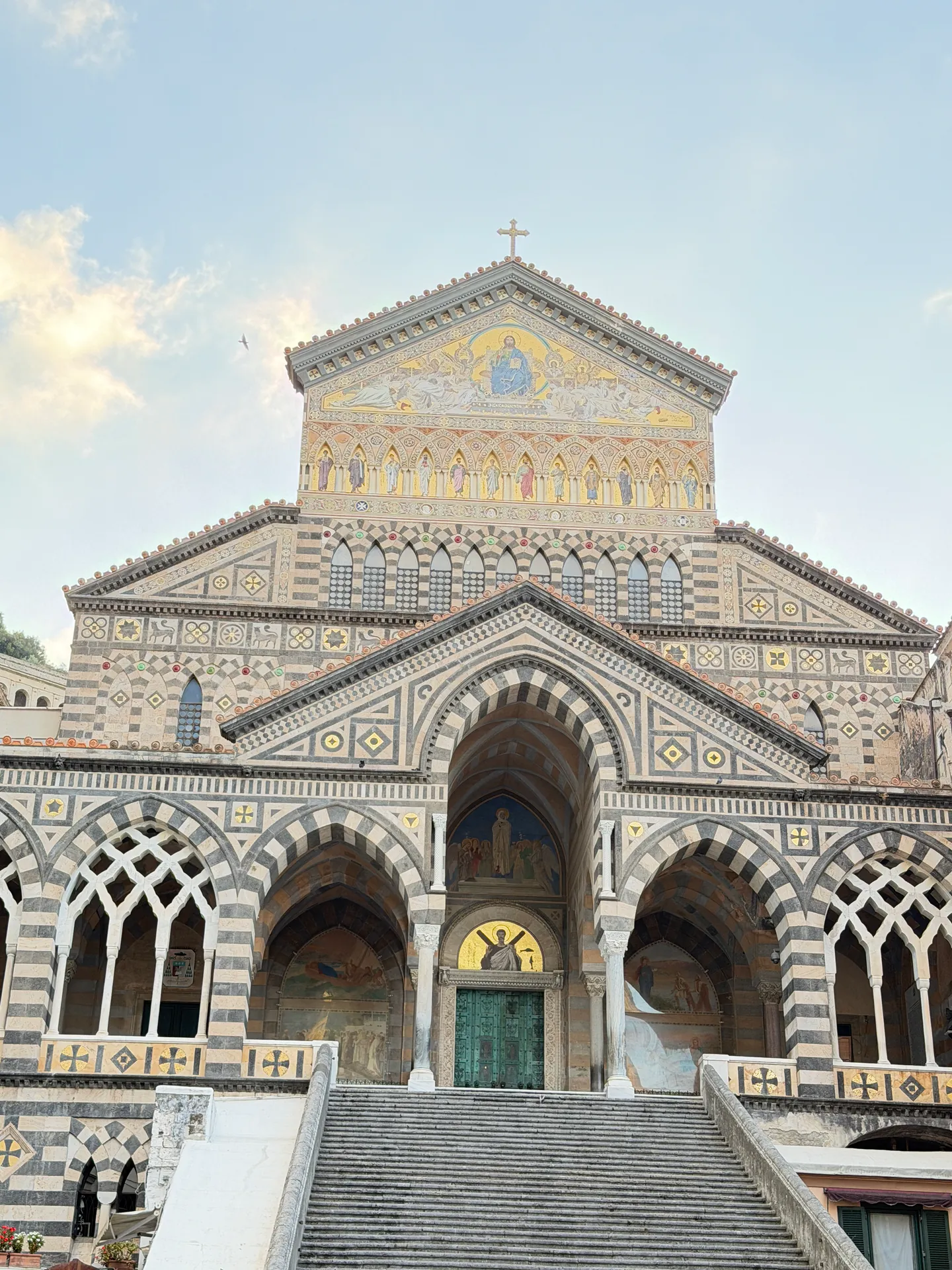 Wide stone staircase rising to the striped facade and bronze door of Amalfi cathedral
