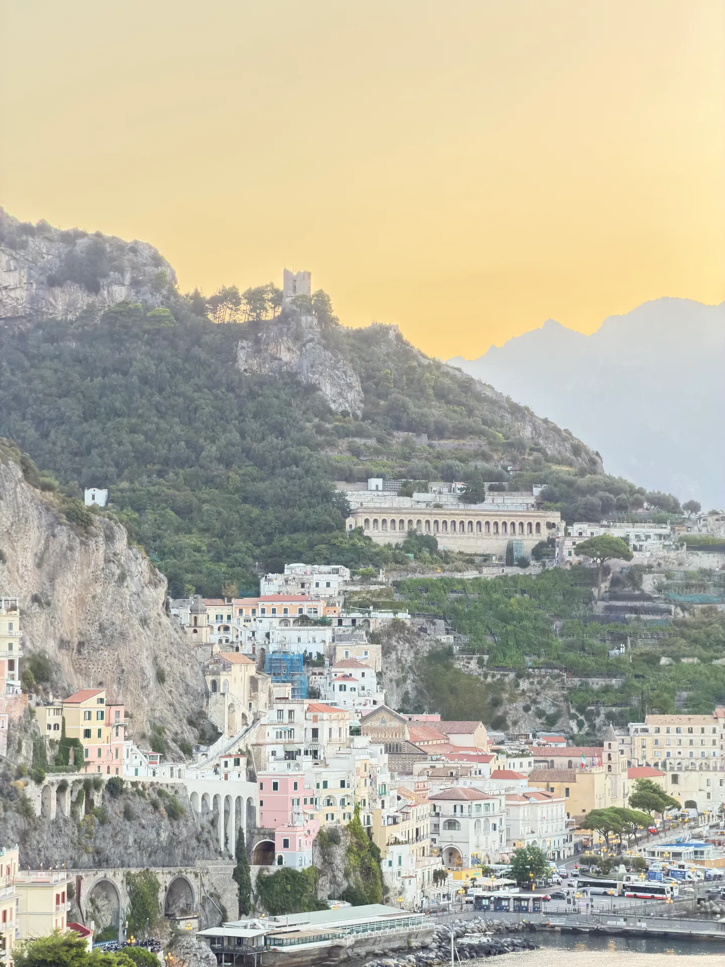 Amalfi town and harbour at dawn from above, houses stacked on the hillside under a pale sky