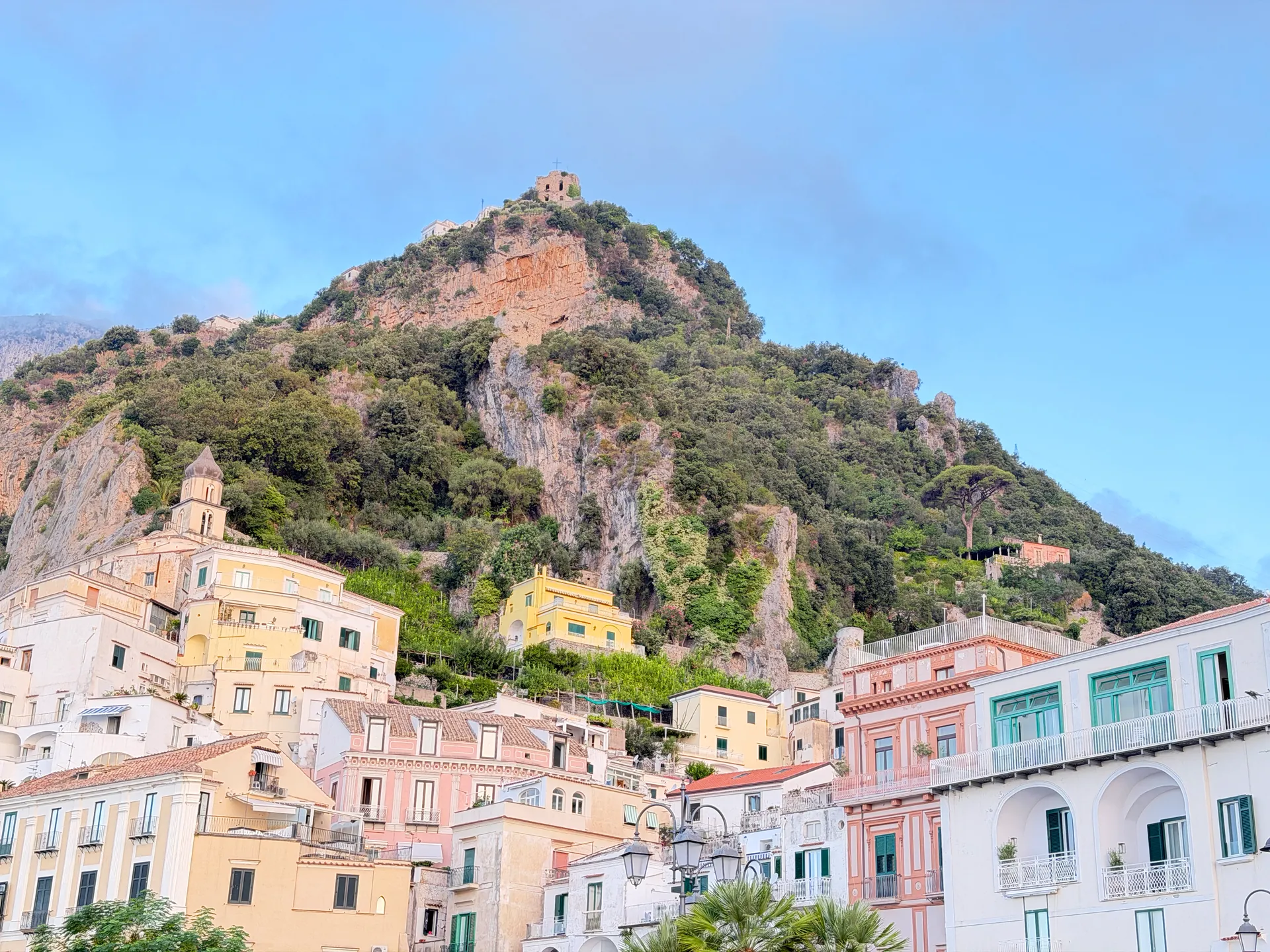 Pastel houses and the spired bell tower of San Benedetto below a rocky crag with a ruined square tower on its summit