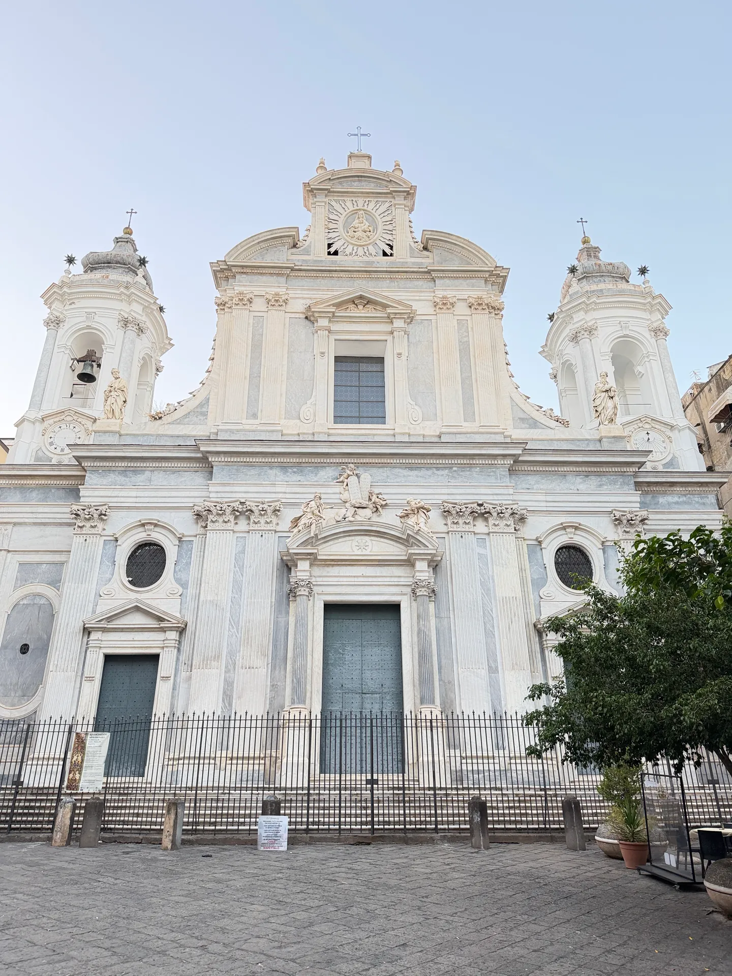 The facade of the Girolamini behind railings, a clock on one tower and a sundial on the other