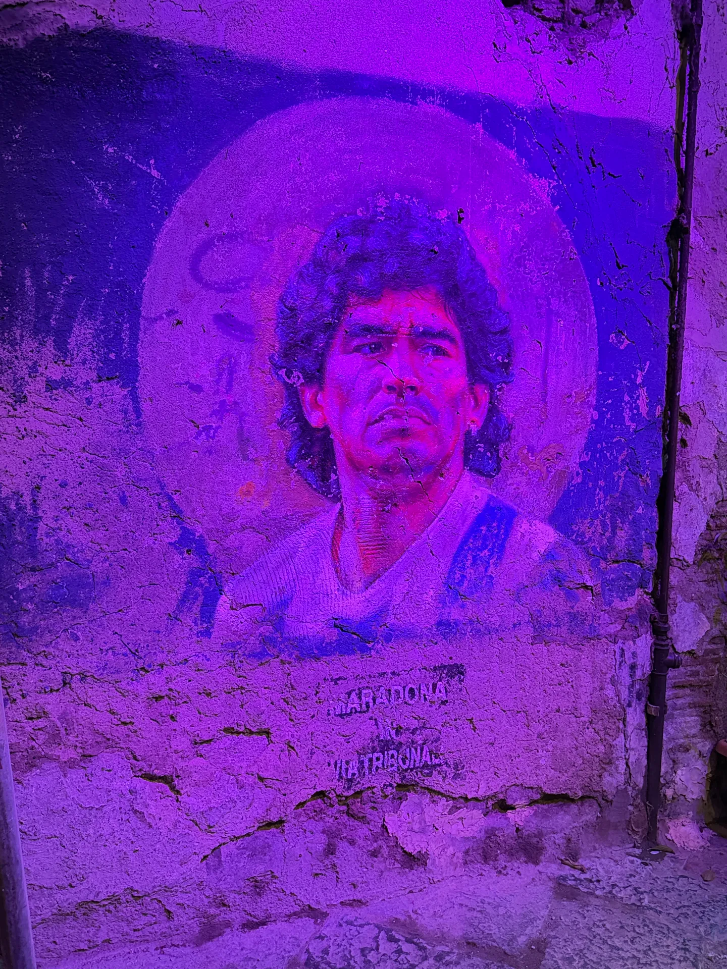 A painted mural lit purple on a wall of Via Tribunali, Naples
