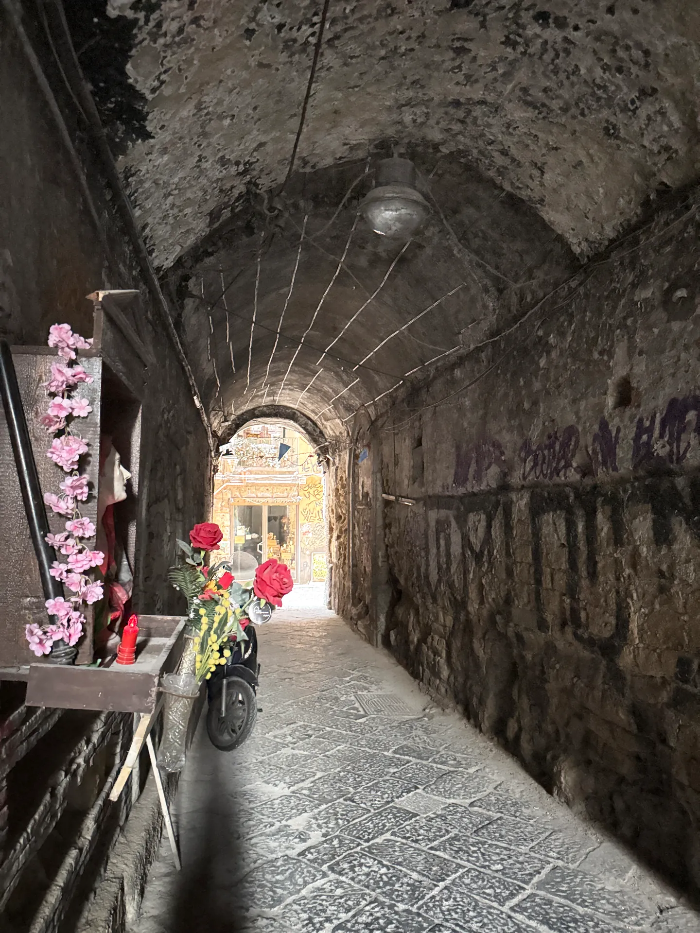 A vaulted passage with a small shrine and flowers at its entrance in Naples