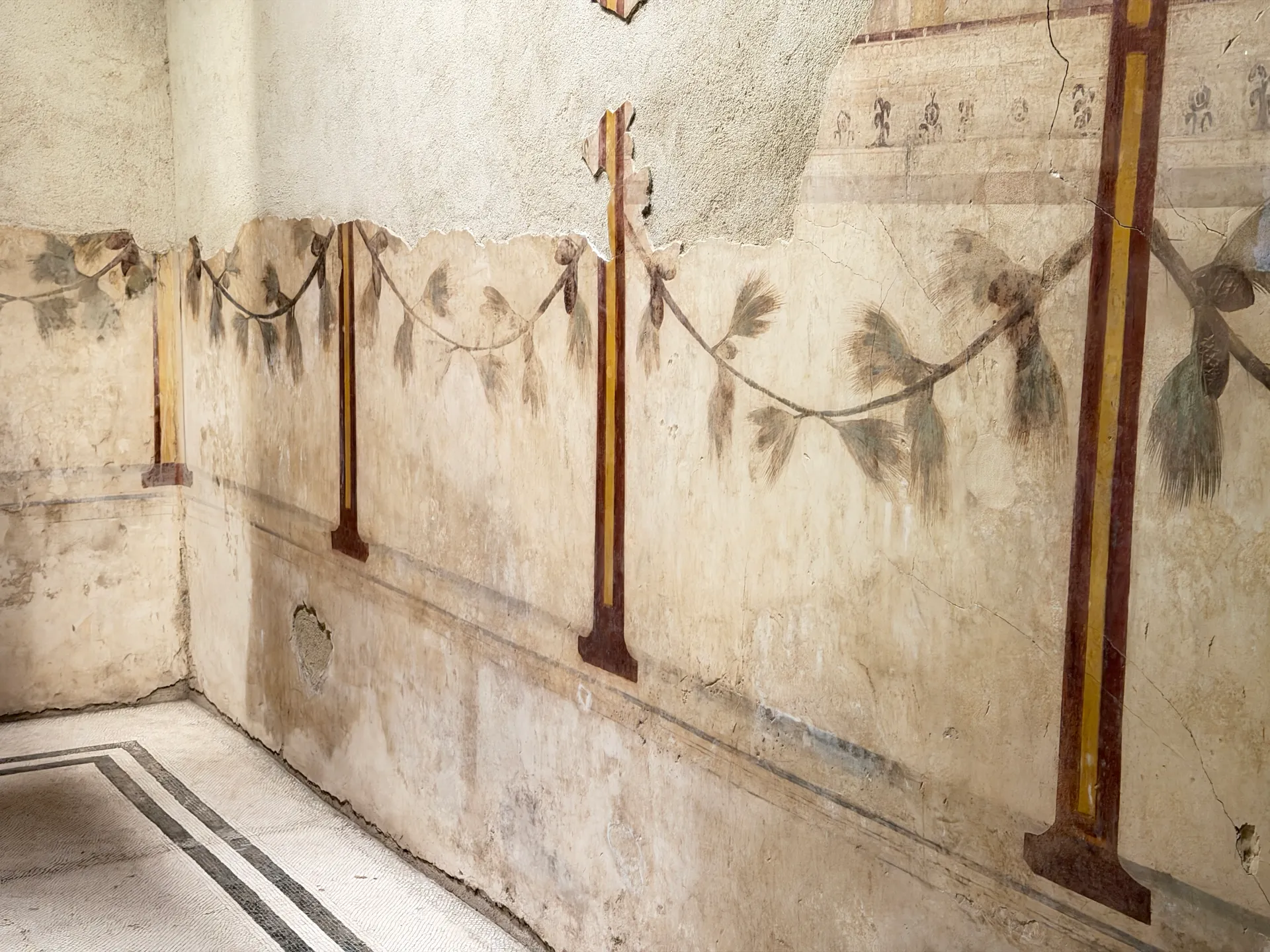 Painted pine garlands swagged between slender red columns on a wall of the House of Augustus.
