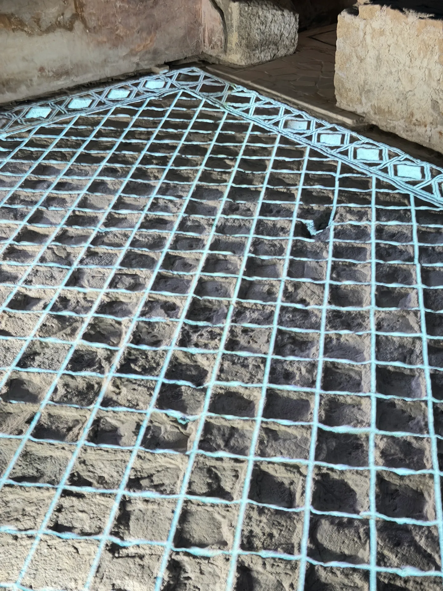 A projected white lattice laid over the rough stone floor of a room in the House of Augustus.